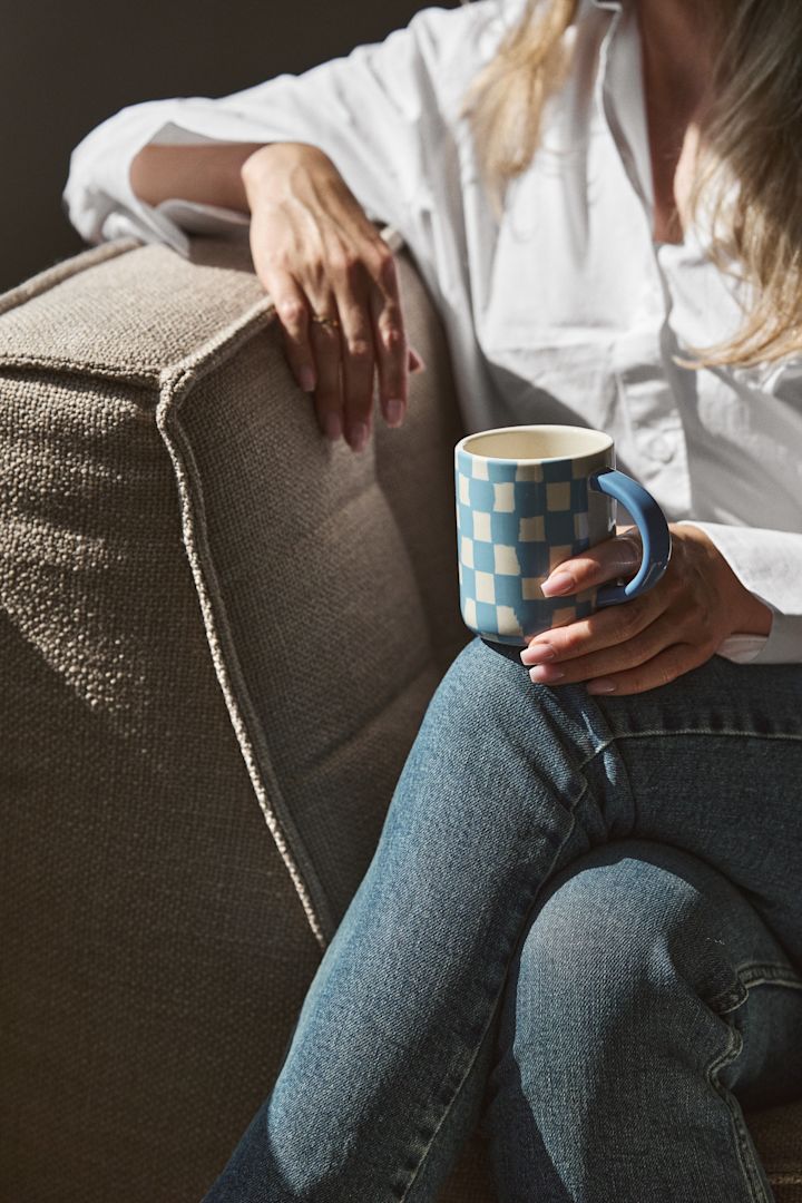 Tern og striber er en af de store trends i efterårets indretningstrends 2024. Her kan du se en kvinde i en lænestol der holder en blåternet kop fra Byon.
