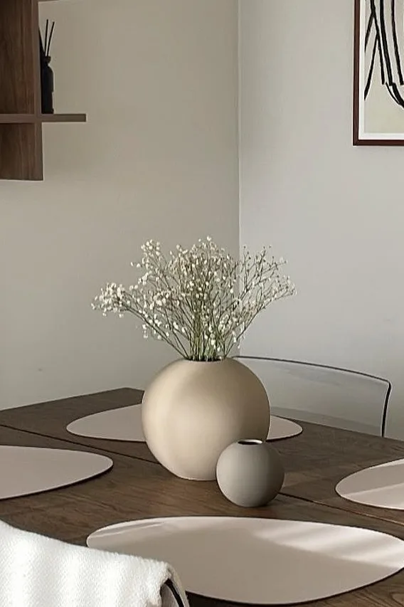 Ball vasen i sand og grå, i to forskellige størrelser der står på et spisebord i en spisestue i neutrale farver.