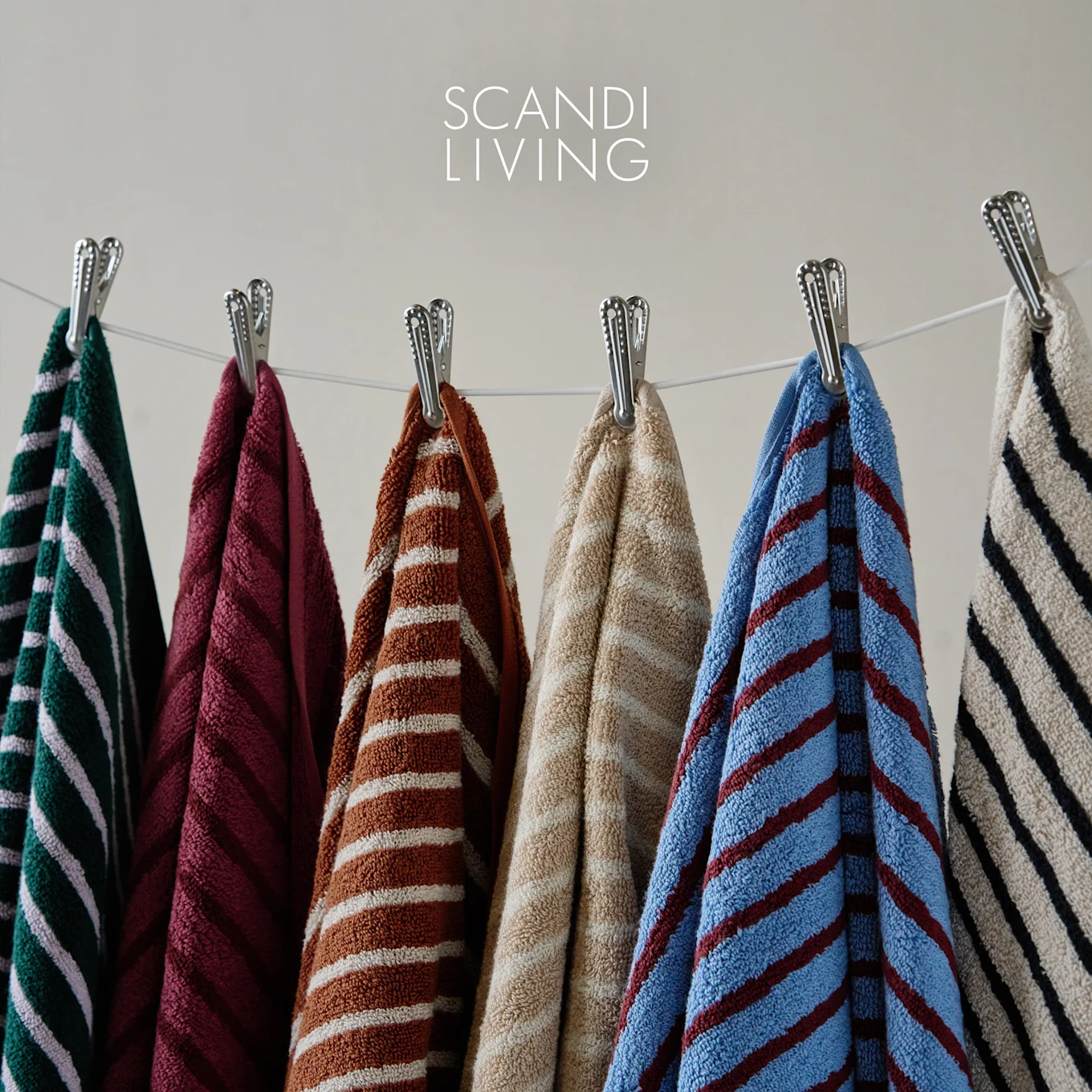 Et udvalg af stribede håndklæder i forskellige farver hængende på en tørresnor, med Scandi Living logo.