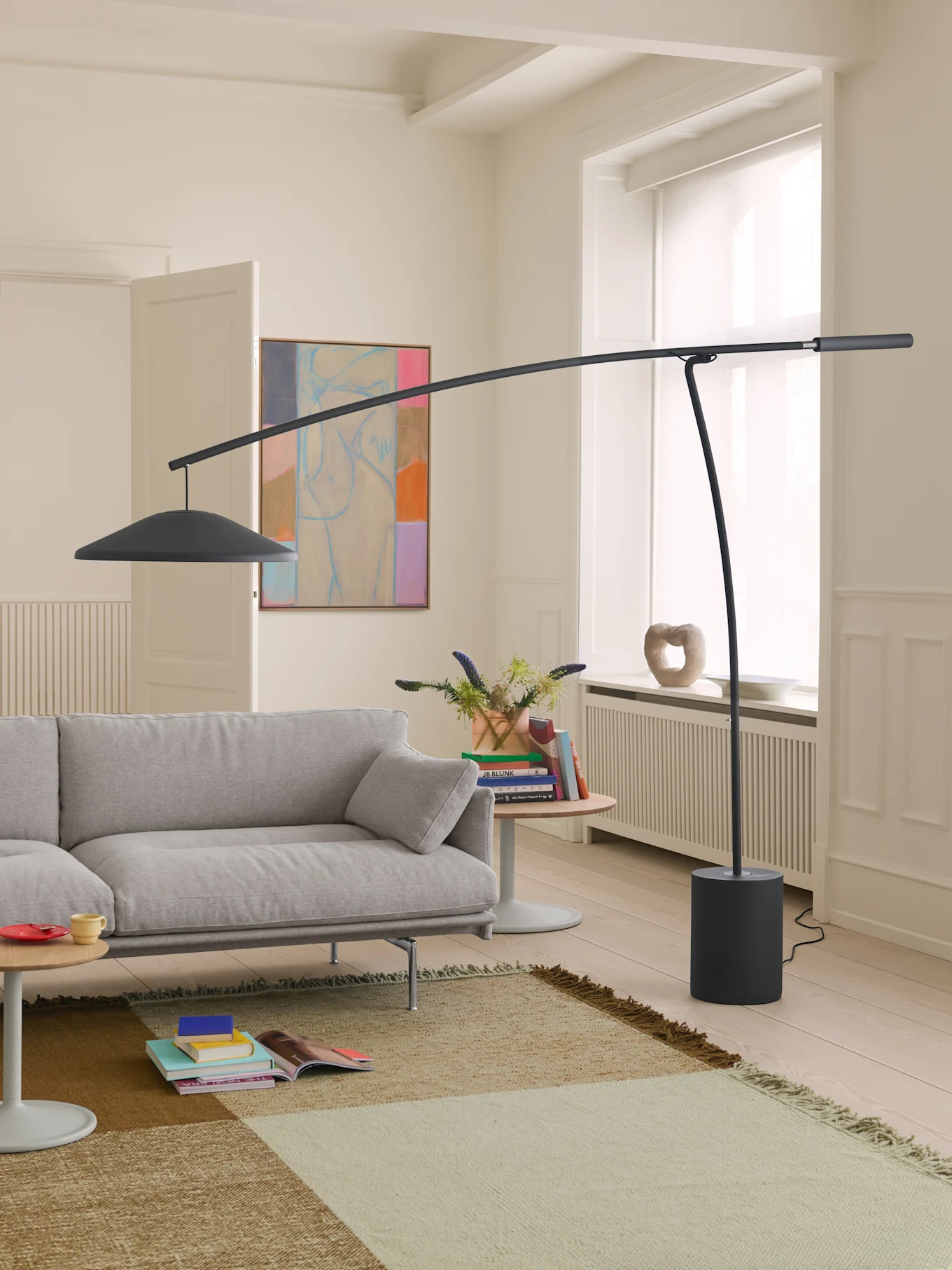En moderne stue med en lysegrå sofa, en høj mørkegrå buet gulvlampe og et mønstret tæppe på lyst trægulv.