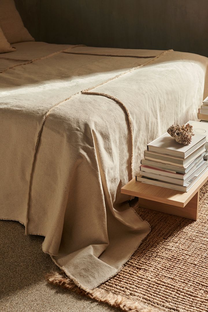 Blød seng dækket med et minimalistisk, beige sengetæppe.