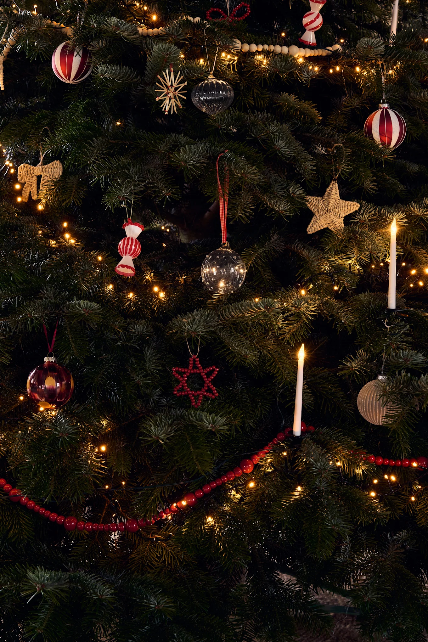 Et rigt dekoreret juletræ med forskellige ornamenter, varme lyskæder og glødende stearinlys.