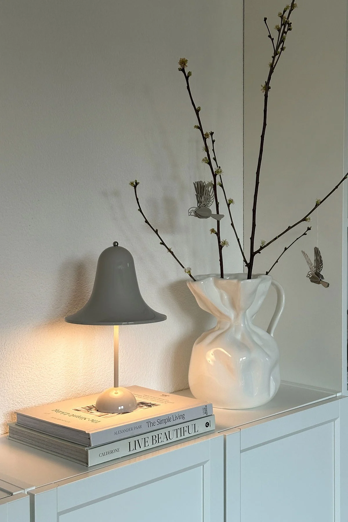 På @oursmall.home kan du se to mulige mors dag-gaver: Pantorp-bordlampen fra Verpan står på en kommode, ved siden af står Crumple-vasen fra Byon med et par kviste i.