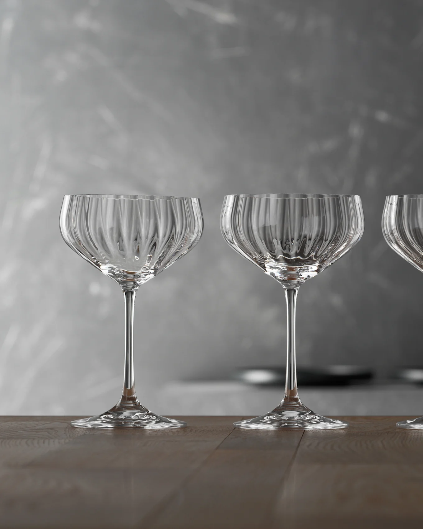 Tre tomme, klare riflede champagneglas på et træbord mod en grå baggrund.