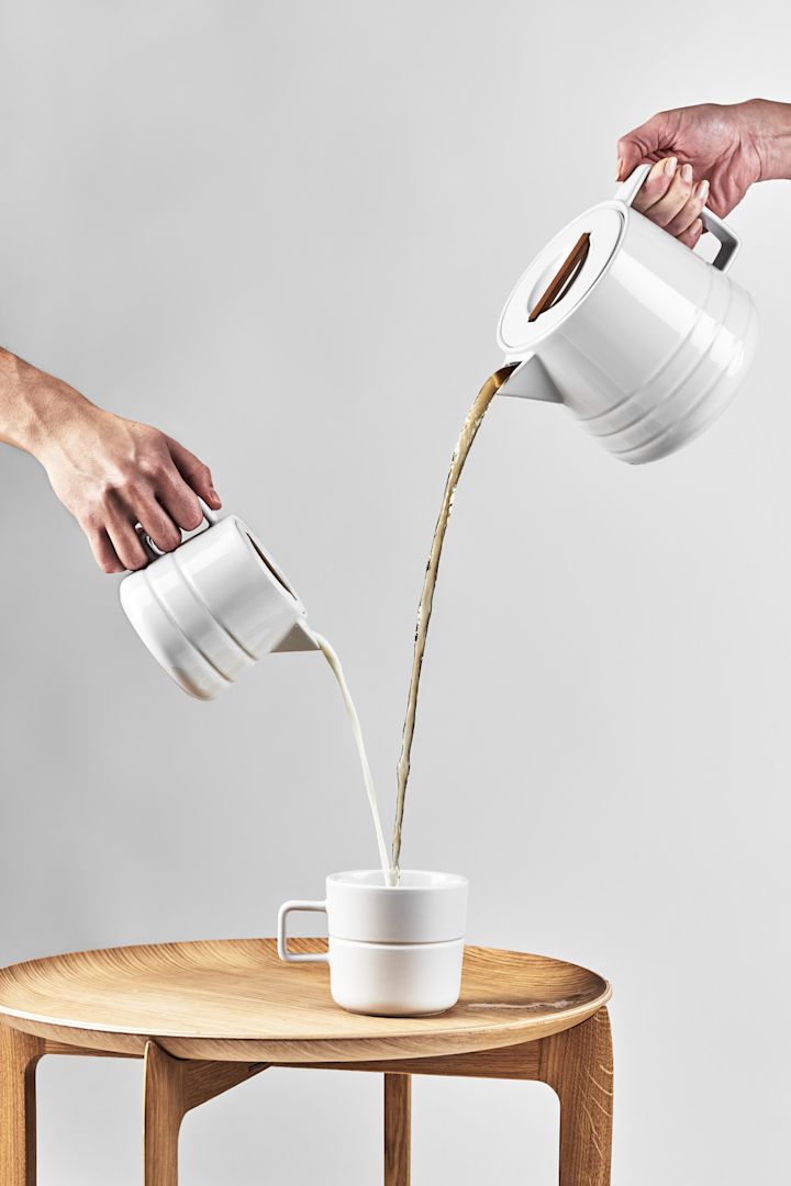 Store kaffekrus: Det hvide Lines-krus fra NJRD står på et sidebord, mens kaffe og mælk skænkes fra de tilsvarende kander ovenfra.