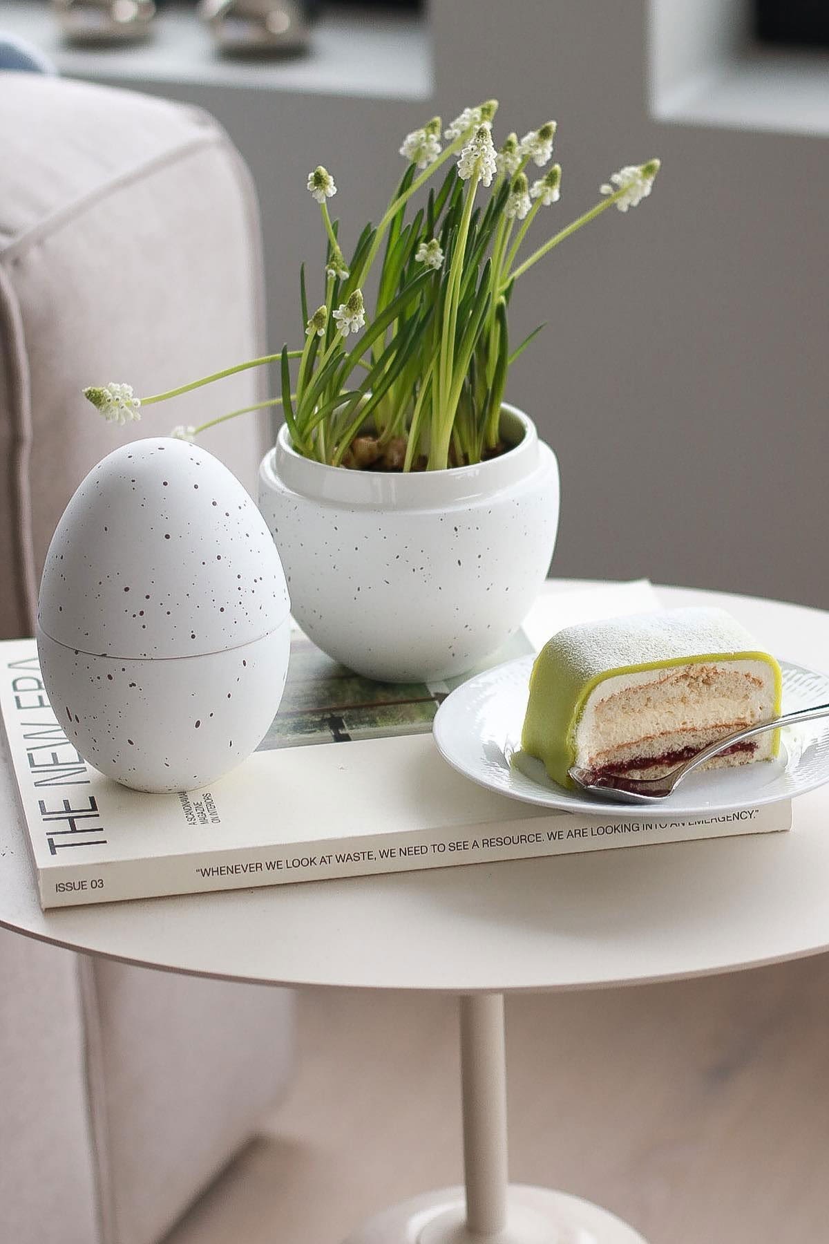 På et sidebord står den hvide bonbonniere med blomster i fra Cooee Design, ved siden af en tallerken med Princesstarta, hjemme hos @picsbyellen.