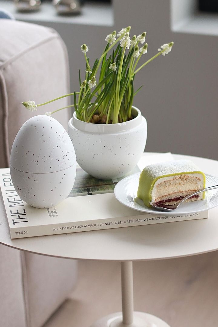 På et sidebord står den hvide bonbonniere med blomster i fra Cooee Design, ved siden af en tallerken med Princesstarta, hjemme hos @picsbyellen.