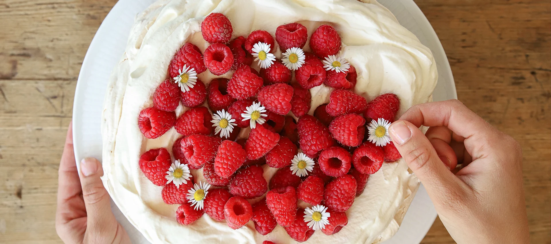 Her ses en fin flødekage sækket med friske hindbær og spiselige blomster ovenfra.