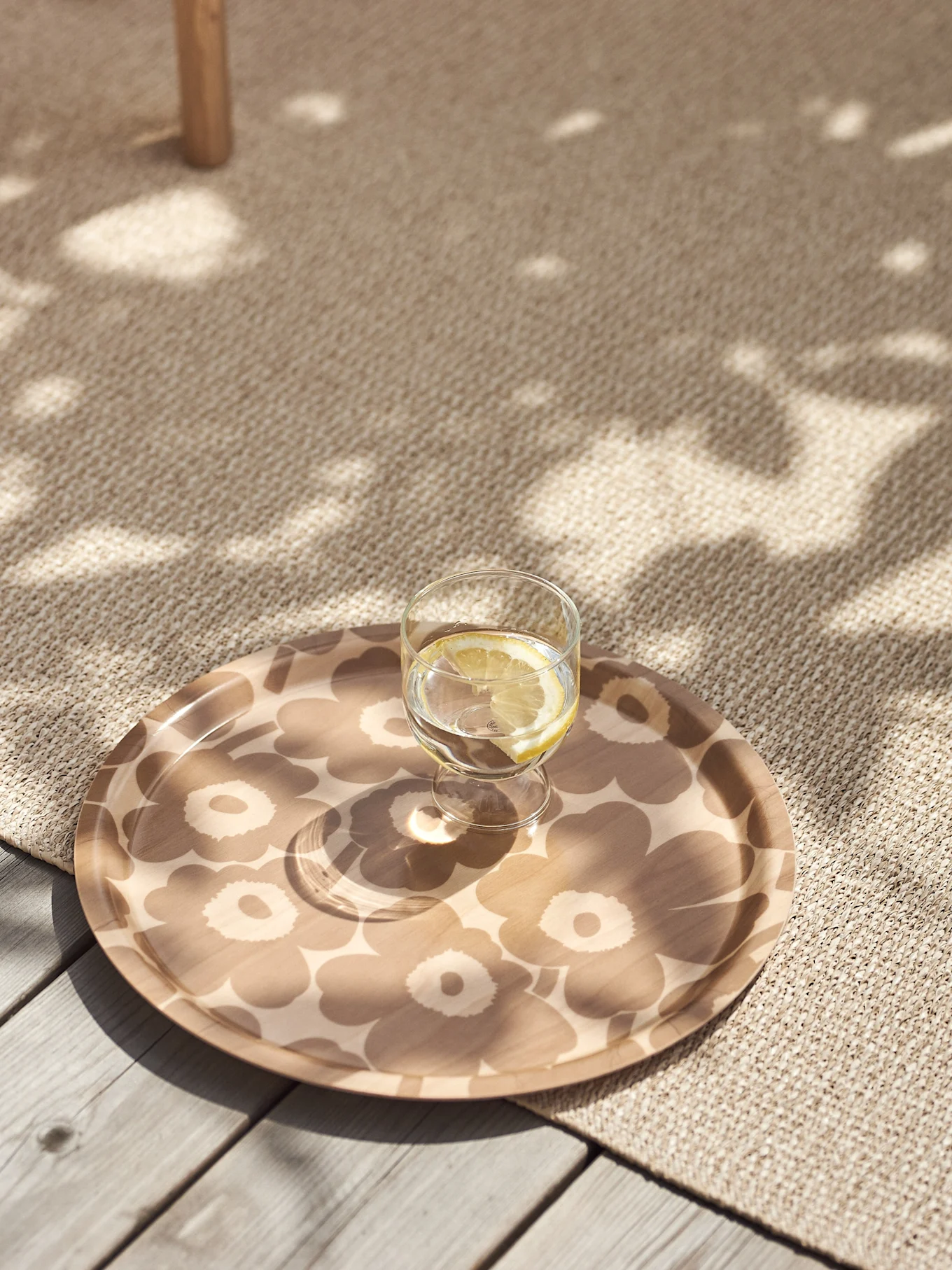 Glas citronvand på en beige blomstermønstret bakke på et tekstureret tæppe med plettet sollys.