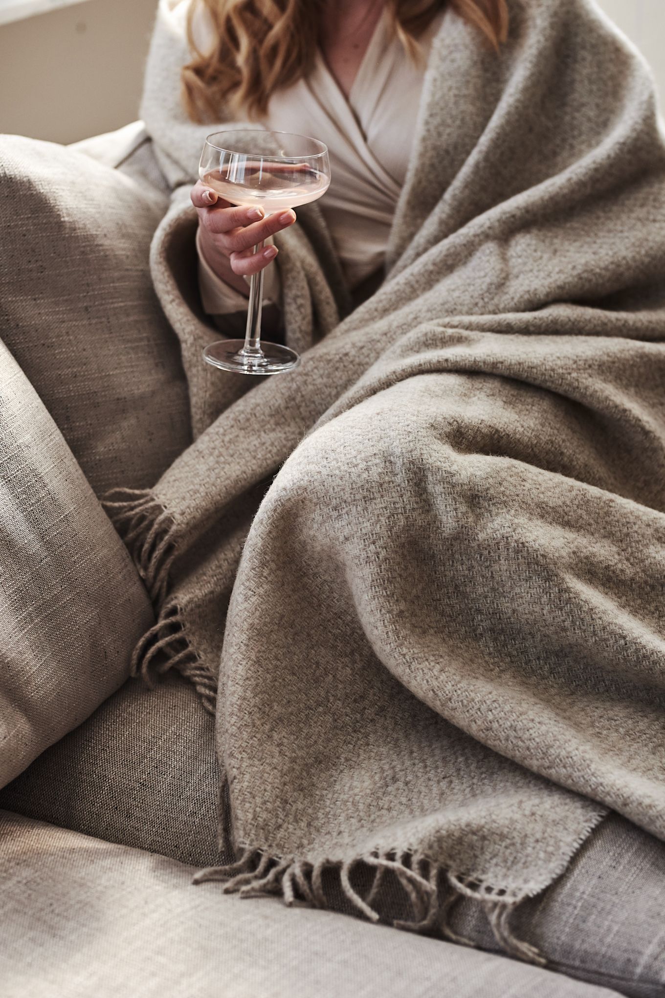 En kvinde er pakket ind i det beige Sandstone uldplaid fra Scandi Living.