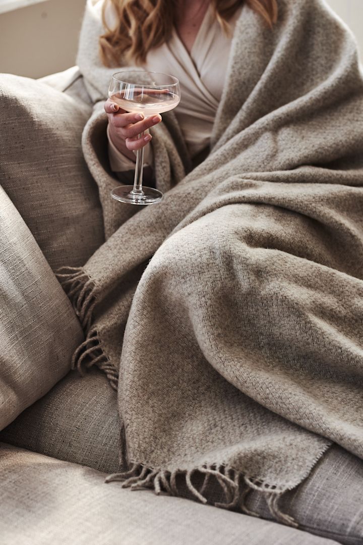 En kvinde er pakket ind i det beige Sandstone uldplaid fra Scandi Living.