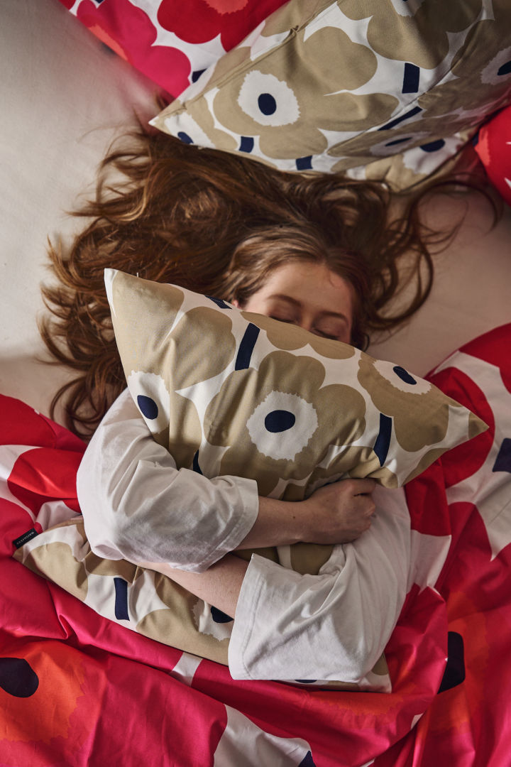 En kvinde krammer Unikko puden i en seng omringet af Unikko sengetøj i rød og pink.