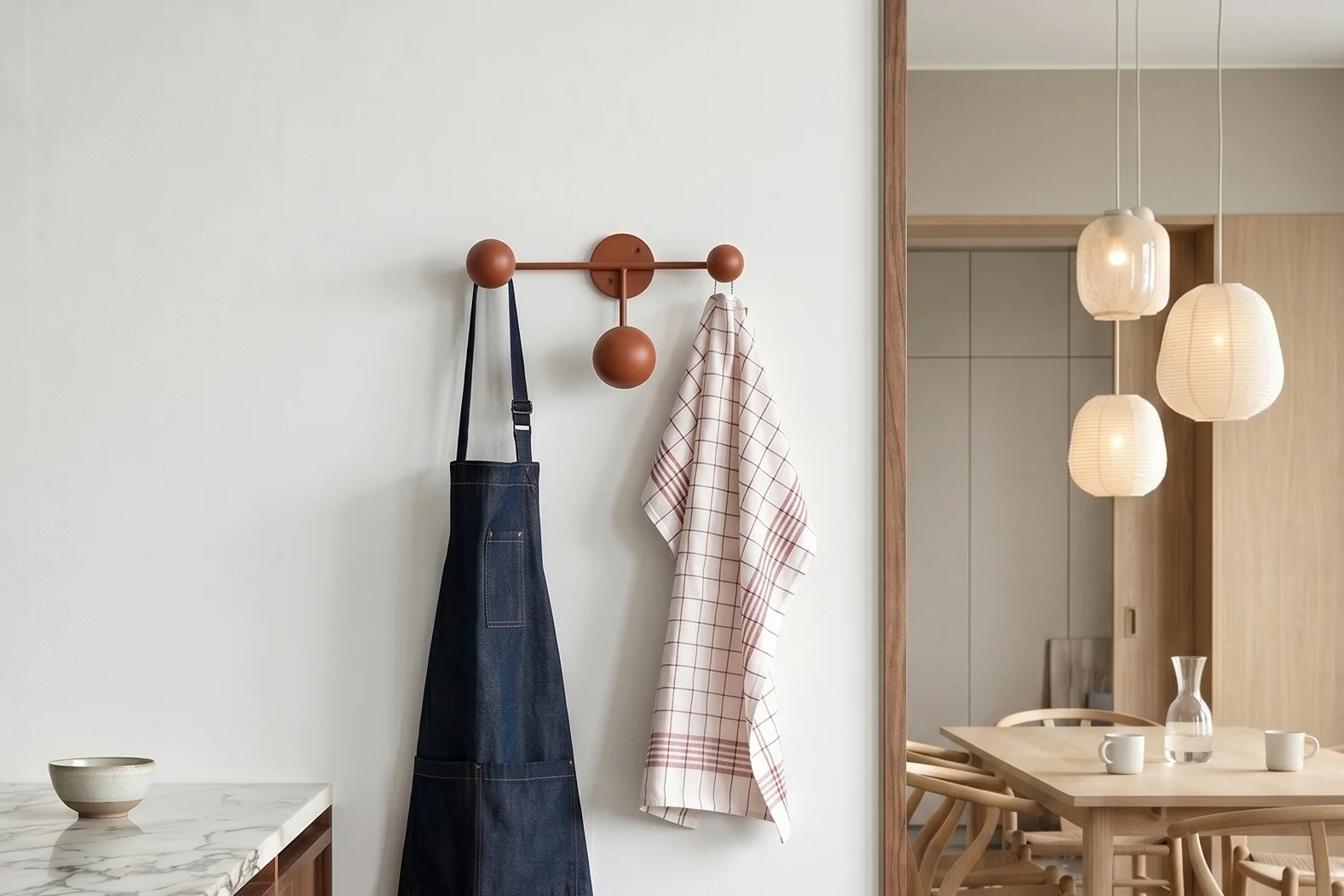 Køkken med marmor. Blå forklæde, ternet viskestykke på knagerække. Spisestue med bord og pendellamper.