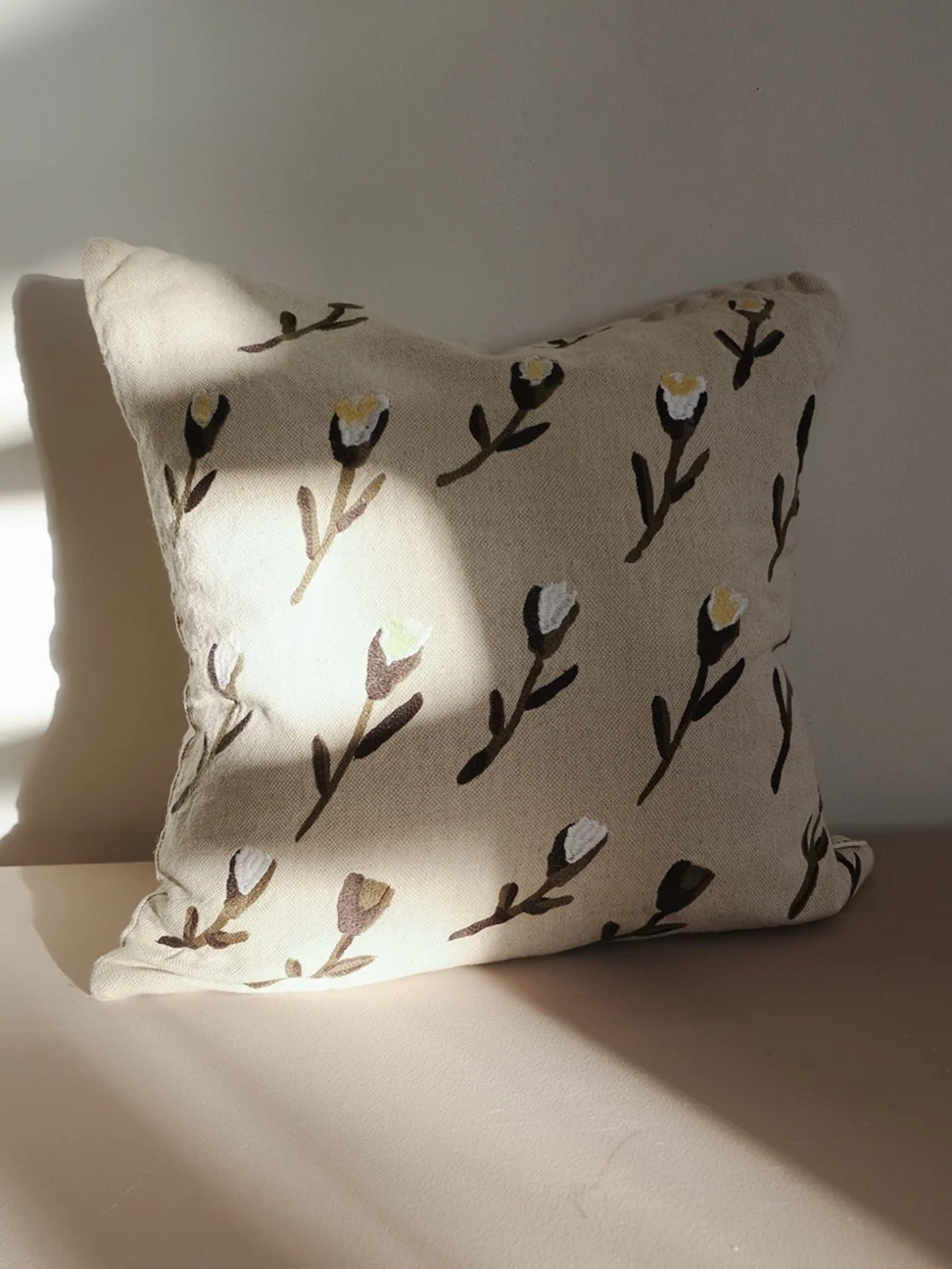 Lys beige pude med et mønster af stiliserede mørkebrune og hvide blomster.