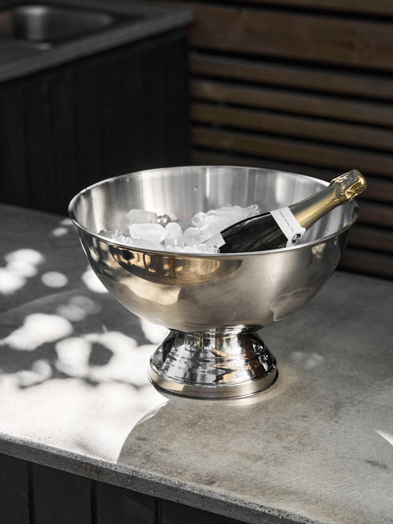 Champagneflaske afkøles i en isspand af rustfrit stål på en betonoverflade.