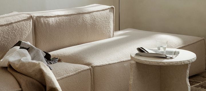 Beige stue med en sofa, sidebord og en hyggelig plaid fra Ferm Living.