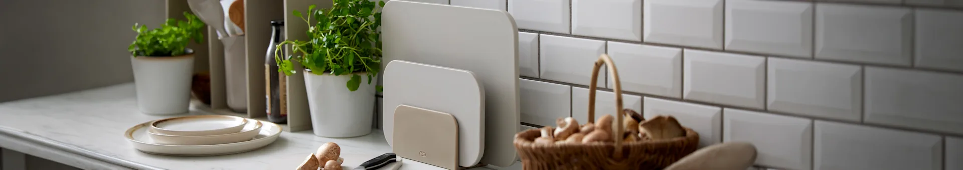 To beige skærebrætter i en holder på et køkkenbord med andre køkkenredskaber.