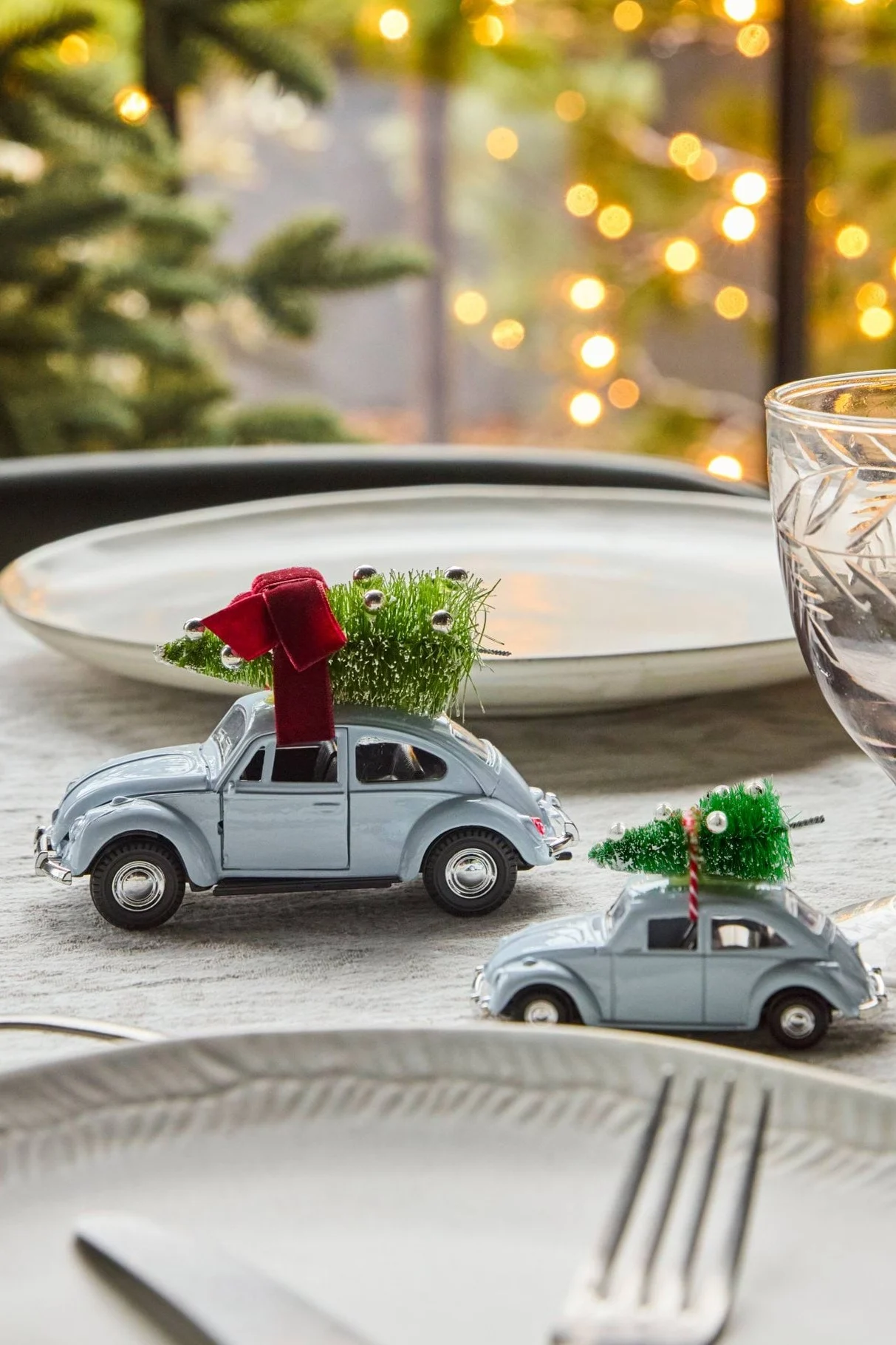 Et flat lay viser gyldne julepynt (træ, agern, fugl, bolsjestok, slik), grå mønstrede servietter og en hvid vase med en gren på træ.