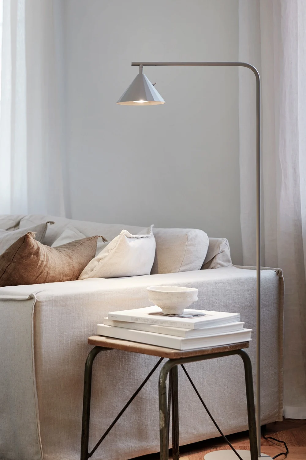 En hyggelig stue med en lys linnedsofa, en gulvlampe og et sidebord med bøger og en skål.