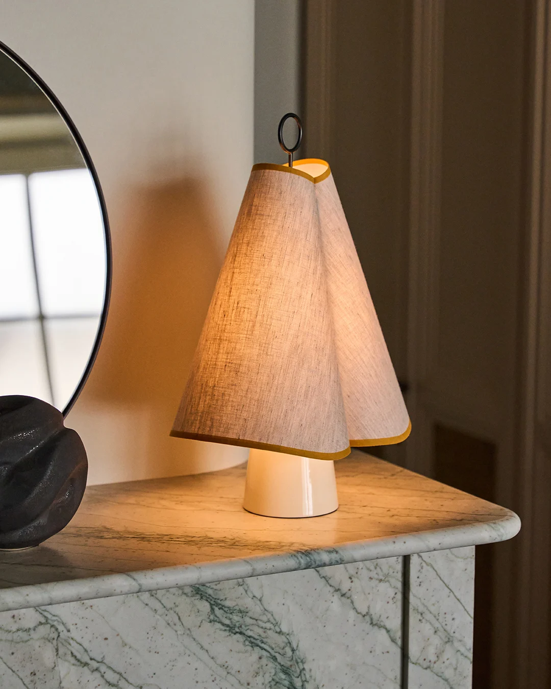 En unik bordlampe med en dobbelt konisk stofskærm trimmet i gul, der kaster et varmt skær på en grøn marmorplade.