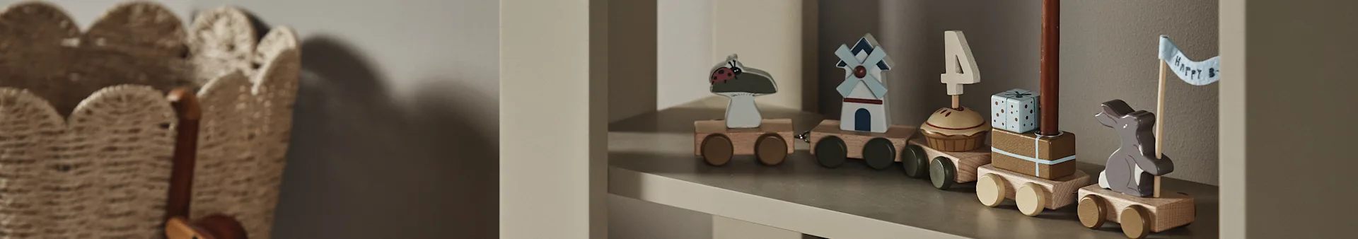 Et trætogsæt på en hylde med vogne med en mariehøne, vindmølle, cupcake med "4"-lys, gave og en kanin med "Happy B"-flag.