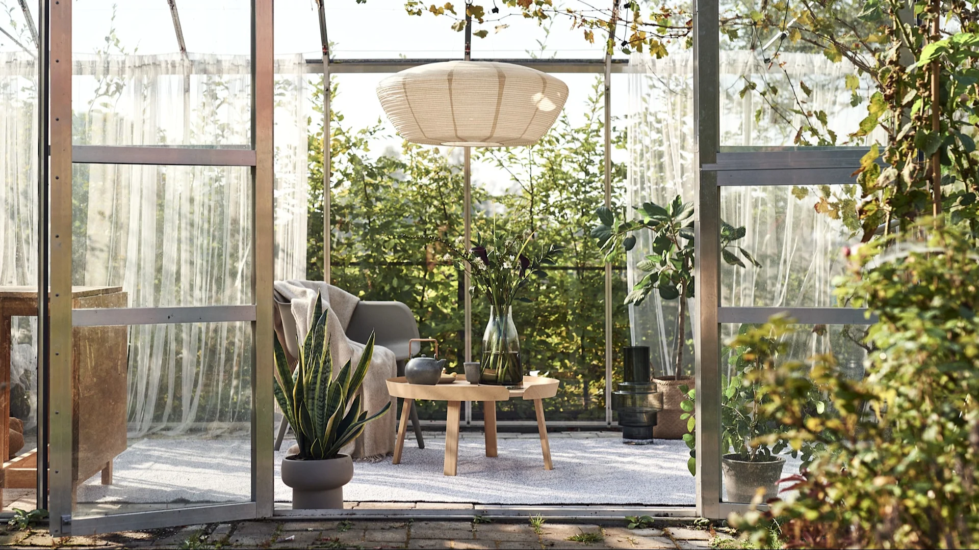 Udendørstæppe: Her ser du et drivhus, som er blevet omdannet til en hyggelig stue med en pendel, en stol, et sidebord og et stort udendørstæppe.