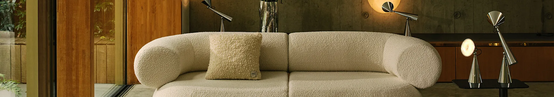 Moderne stue med en råhvid modulsofa i bouclé, et lyst mønstret tæppe og metallamper.