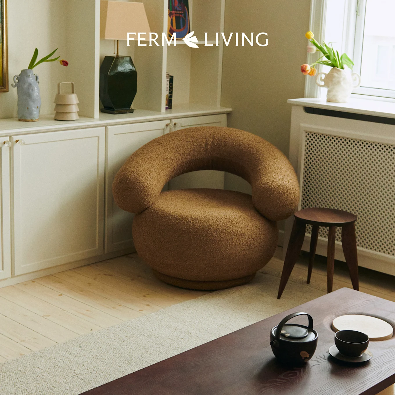 En hyggelig stue med en brun, tekstureret rund lænestol, et træ sofabord med et tesæt og et hvidt skab.