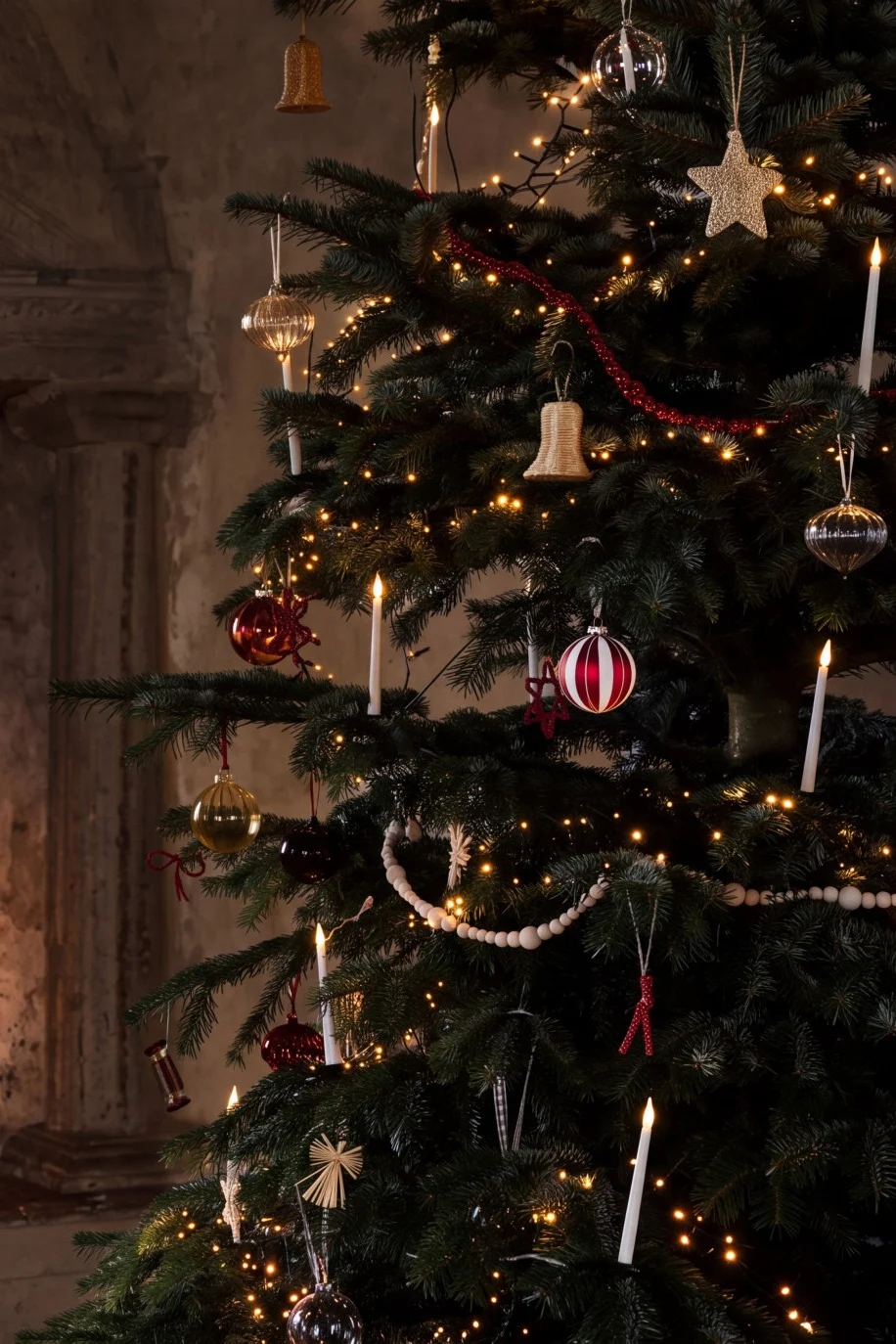 Et pyntet juletræ med lys og kugler ved en hyggelig pejs med brændende ild.