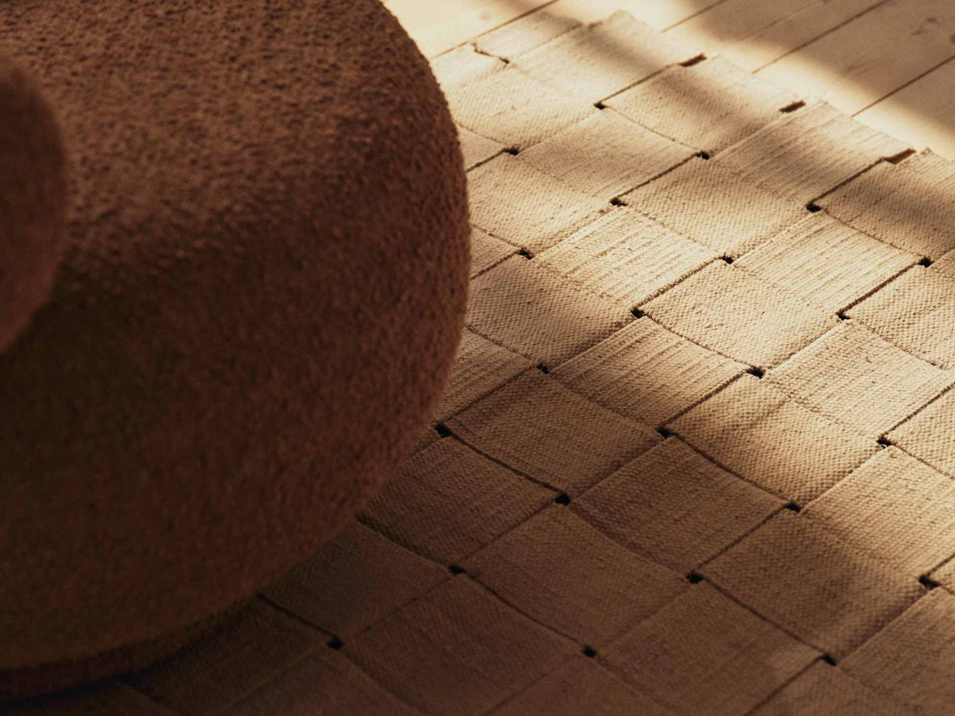 Brun bouclé-møbel, et vævet tæppe og et trægulv med solbeskinnede skygger.