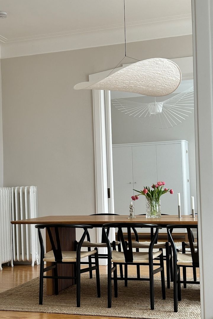 Opdater dit hjem med moderne belysningsideer, her ser du den hængende loftslampe Tense fra New Works hængende over et spisebord med en flok tulipaner. 