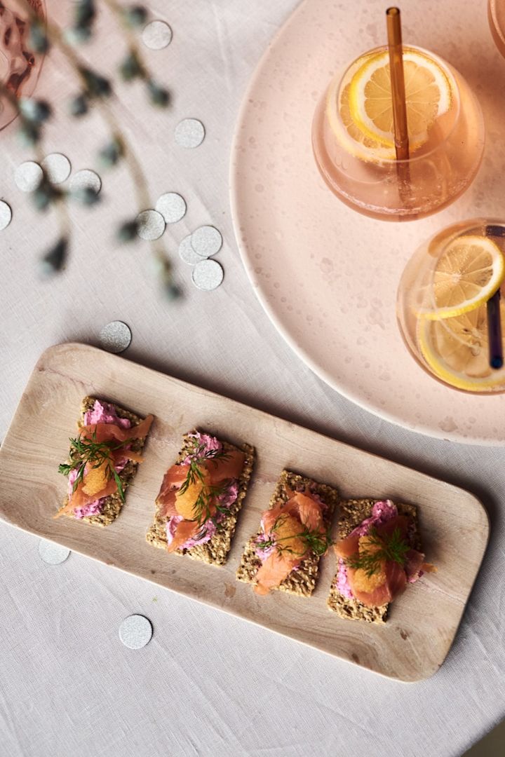 Kanapeer med laks og rødbede, en af de enkle forretter til din nytårsfest på HK Livings lyserøde marmorbakke ved siden af en champagnecocktail.