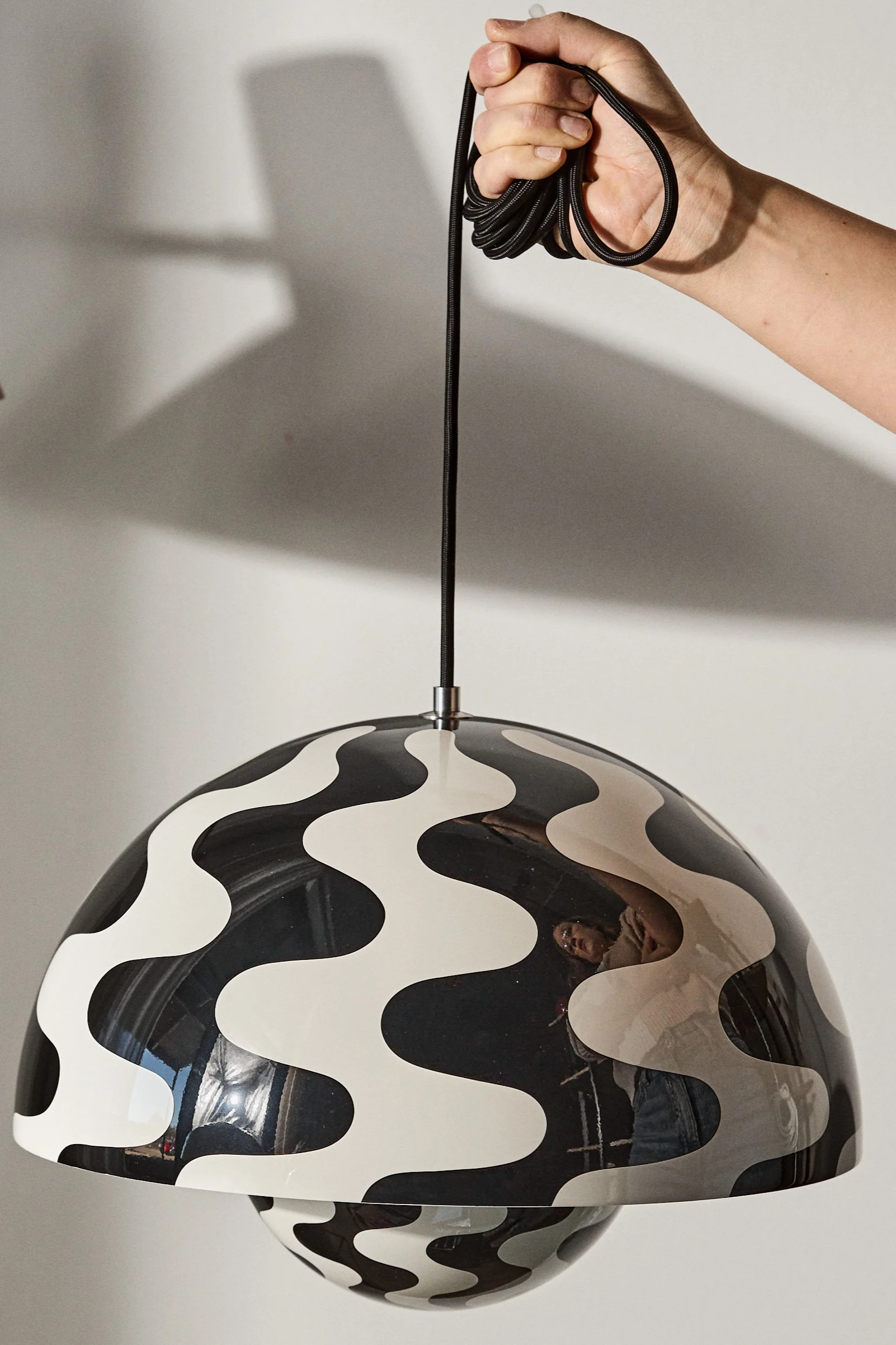 Mønstret loftlamper til stuen kan være en sjov måde at dekorere og lys rummet op. Her kan du se en hånd der holder Flowerpot VP7 loftlampen i et sort og hvidt mønster.