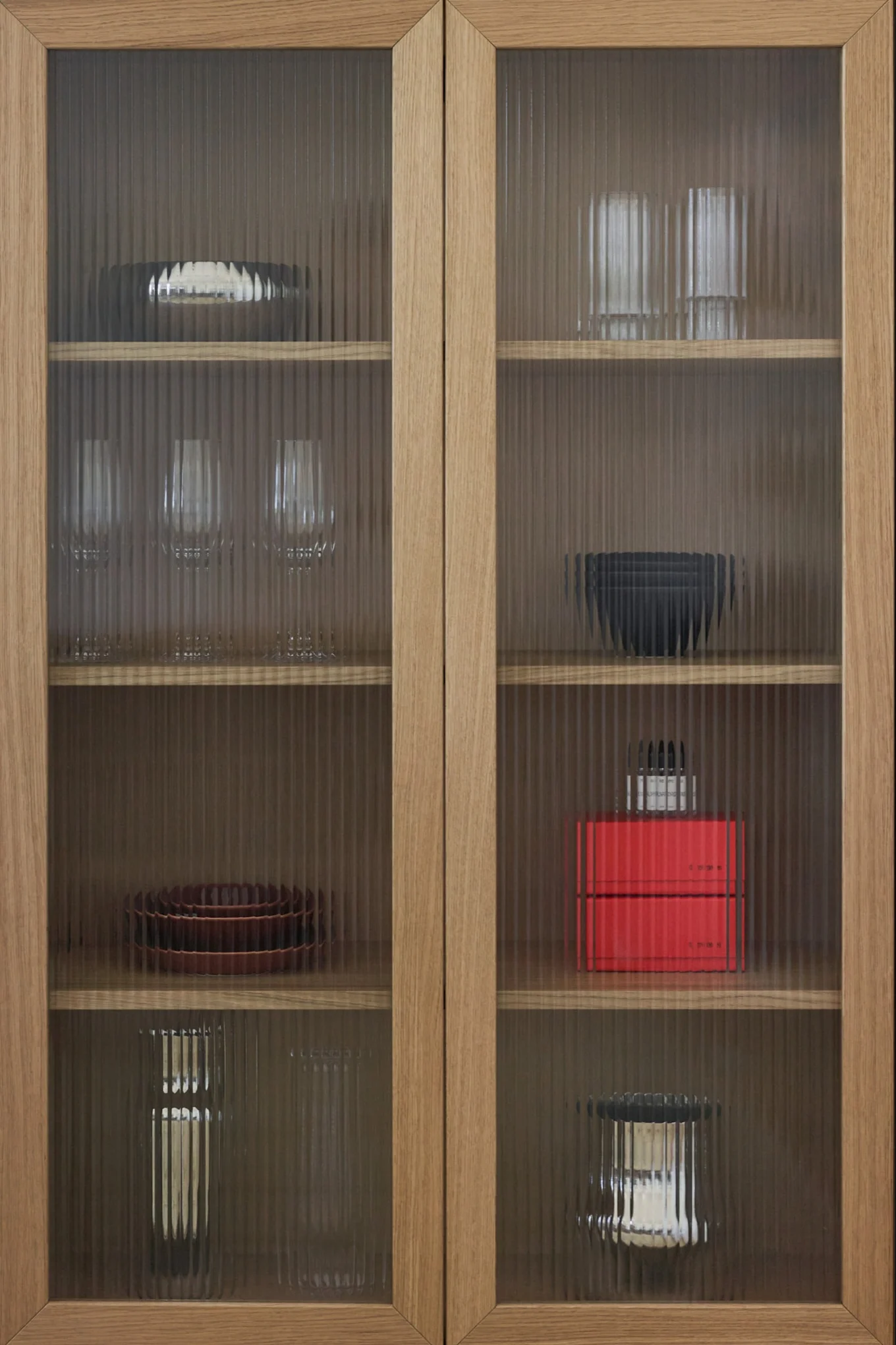 Træskab med riflede glaslåger, der viser forskellige fade, glas og pyntegenstande på hylder.