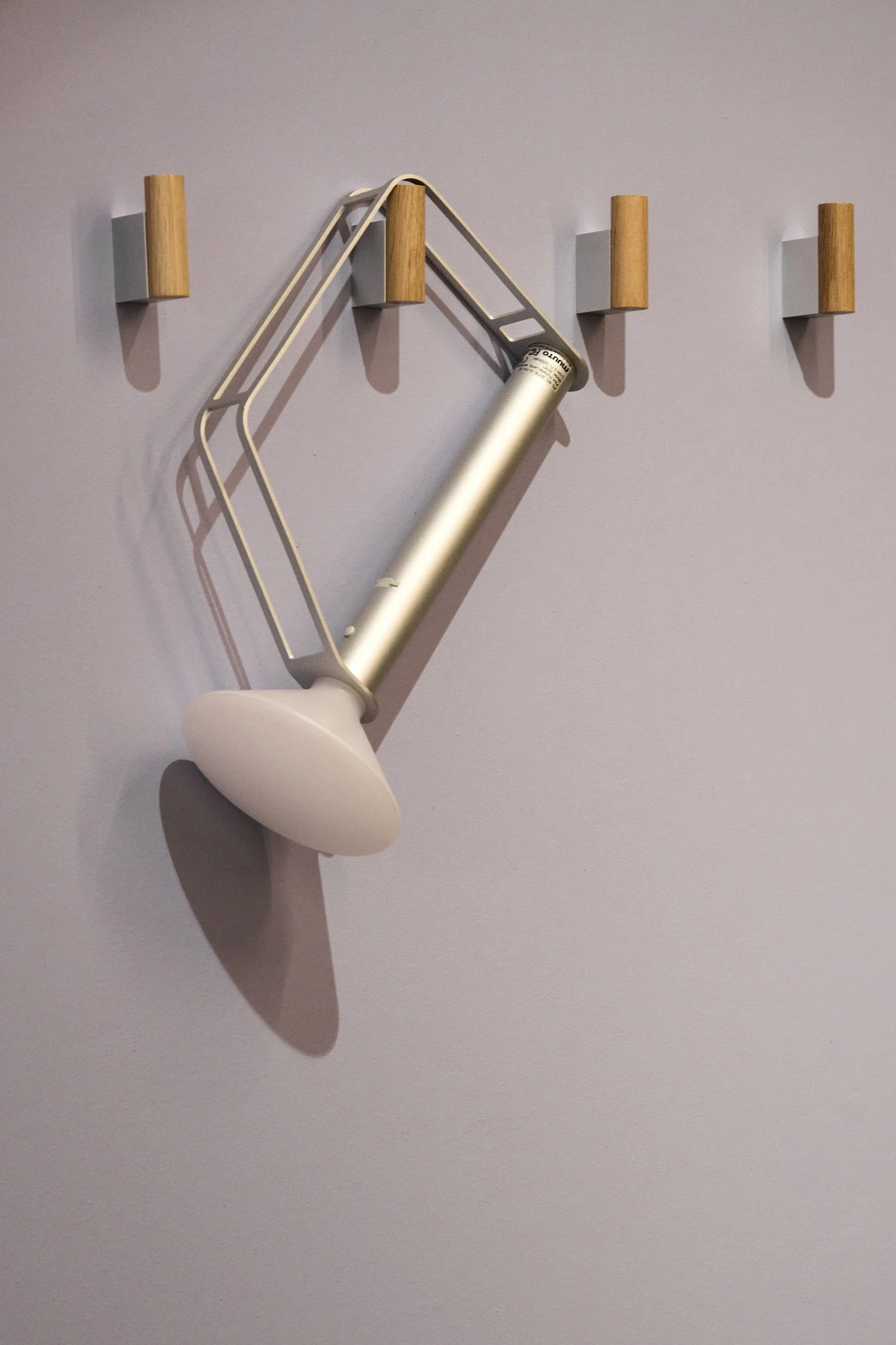 Den sølvfarvede, transportable Piton-bordlampe fra Muuto hænger på en af fire kroge på væggen.