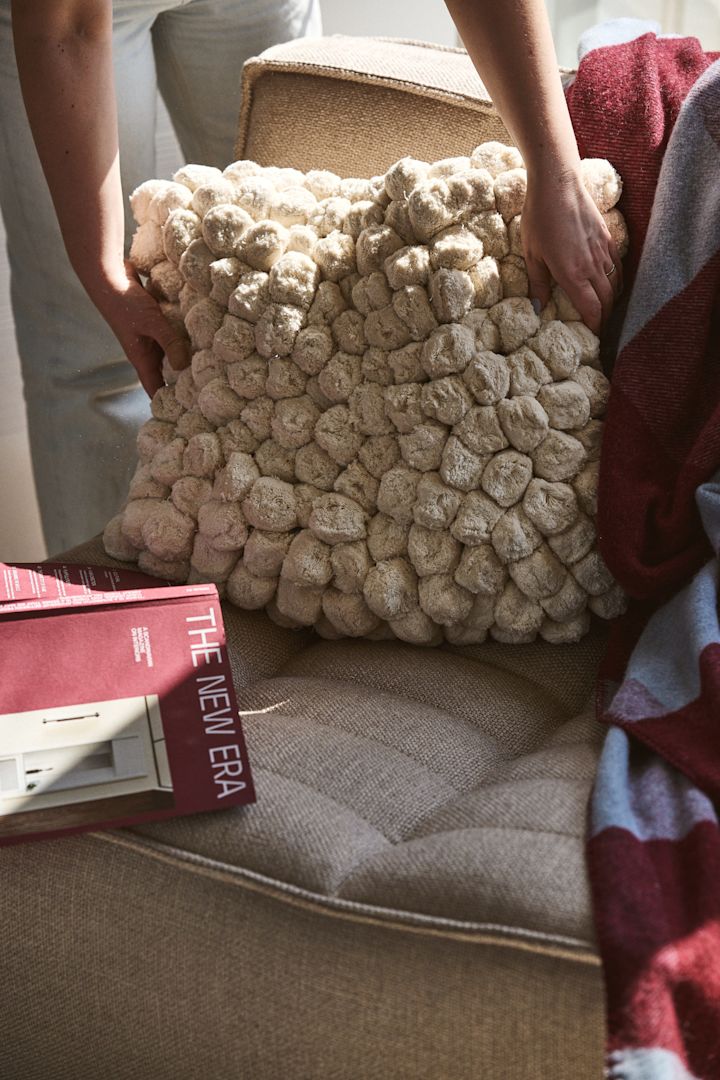 Pom Pom pude fra Byon som placeres i en sofa med et vinrødt tæppe og blåt. Taktile materialer med struktur er en af efterårets indretningstrends 2024.