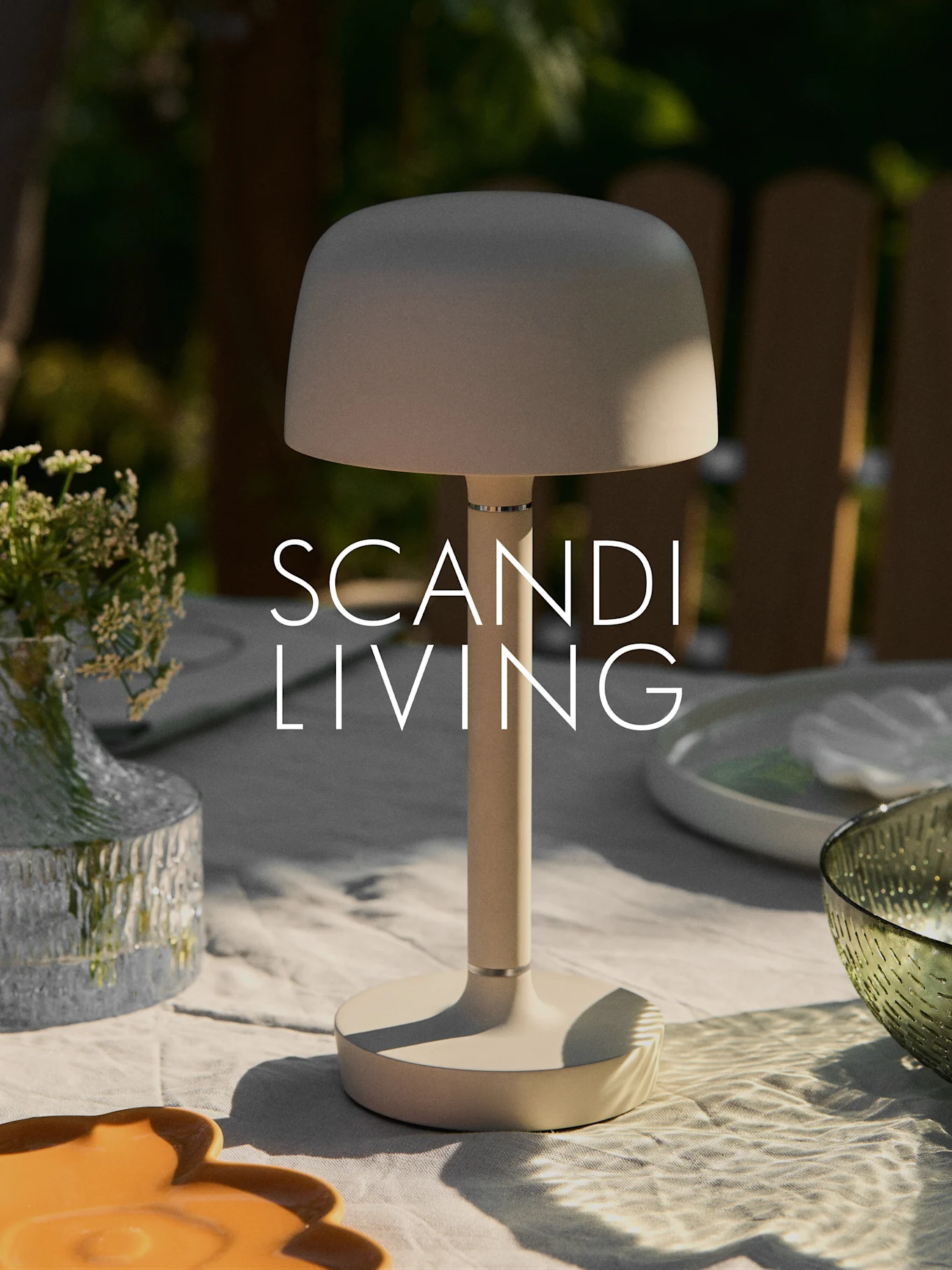 En beige moderne bærbar bordlampe på et udendørs bord med en vase med blomster og fade. "SCANDI LIVING" tekst.