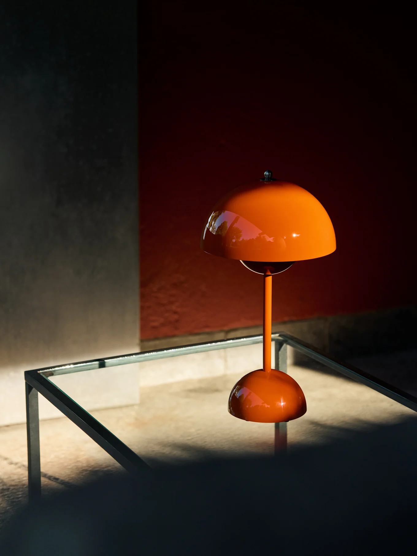 Orange champignonformet bordlampe på et glasbord, der reflekterer grønt.