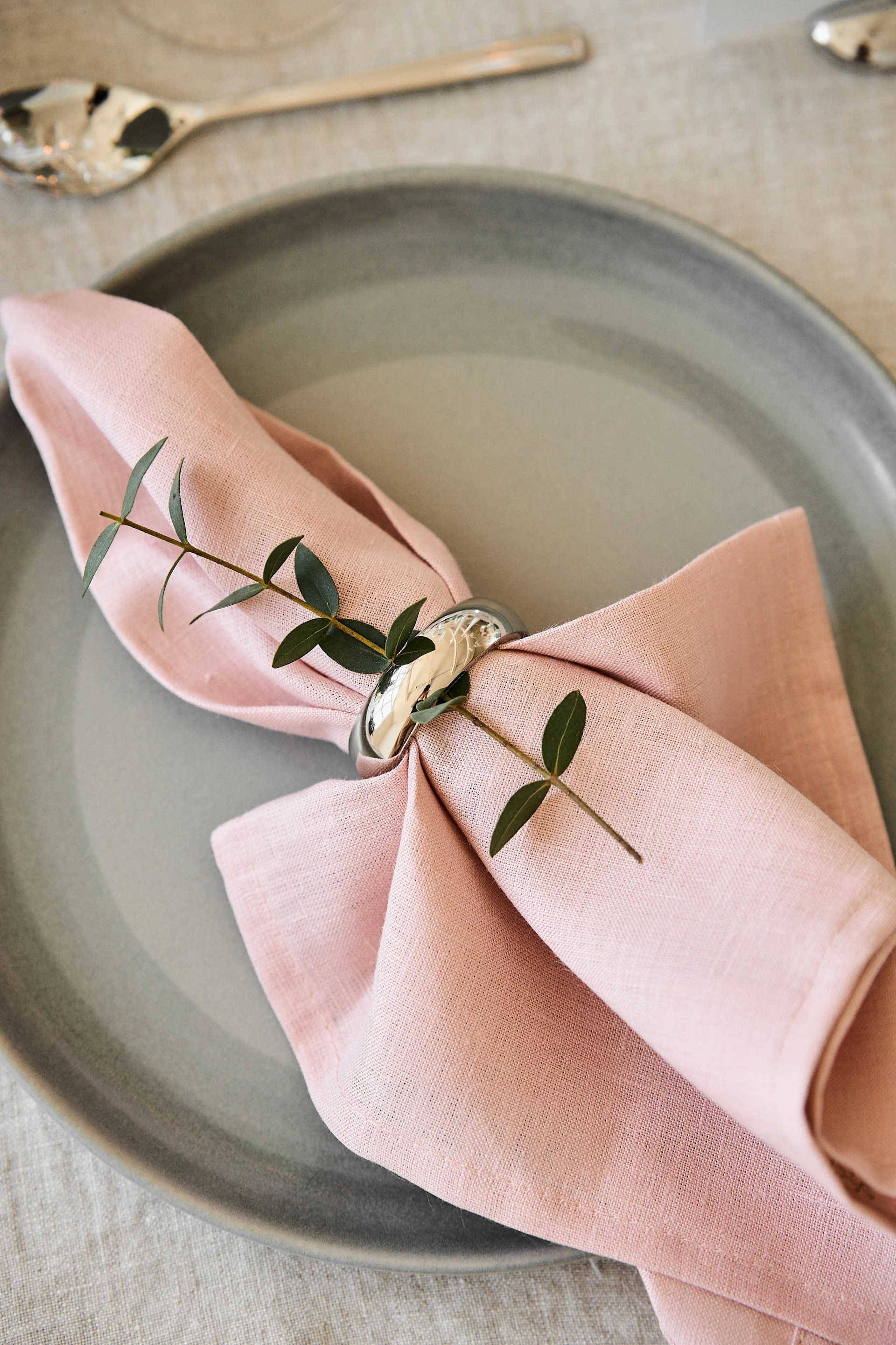 Pynt bordet til dit romantiske måltid derhjemme i behagelige farver. Her ses servietten Clean i Dusty Rose fra Scandi Living liggende på en tallerken med en servietring.