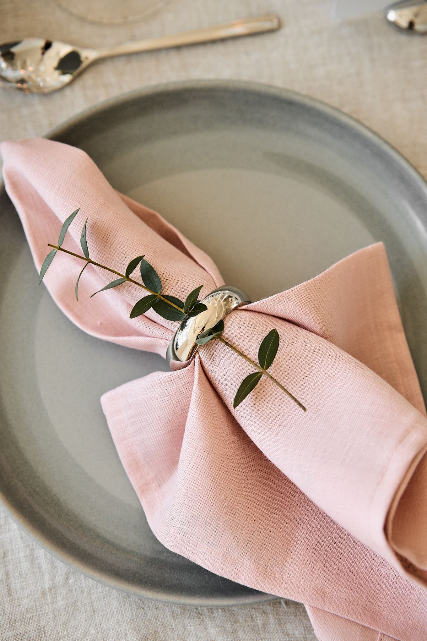 Pynt bordet til dit romantiske måltid derhjemme i behagelige farver. Her ses servietten Clean i Dusty Rose fra Scandi Living liggende på en tallerken med en servietring.