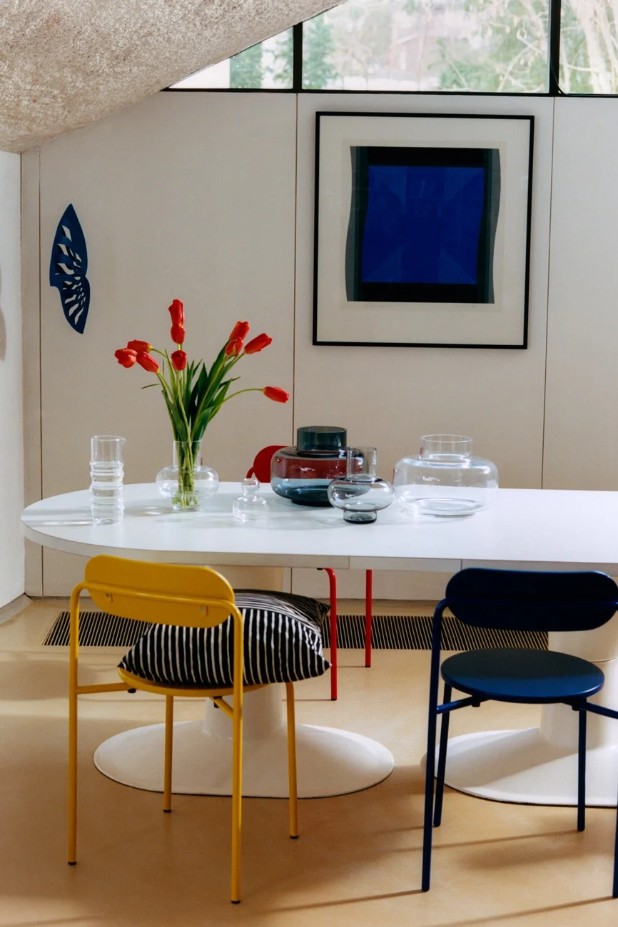 Moderne spisestue med hvidt ovalt bord, røde tulipaner, glasvaser, gule og blå stole og abstrakt blå kunst.