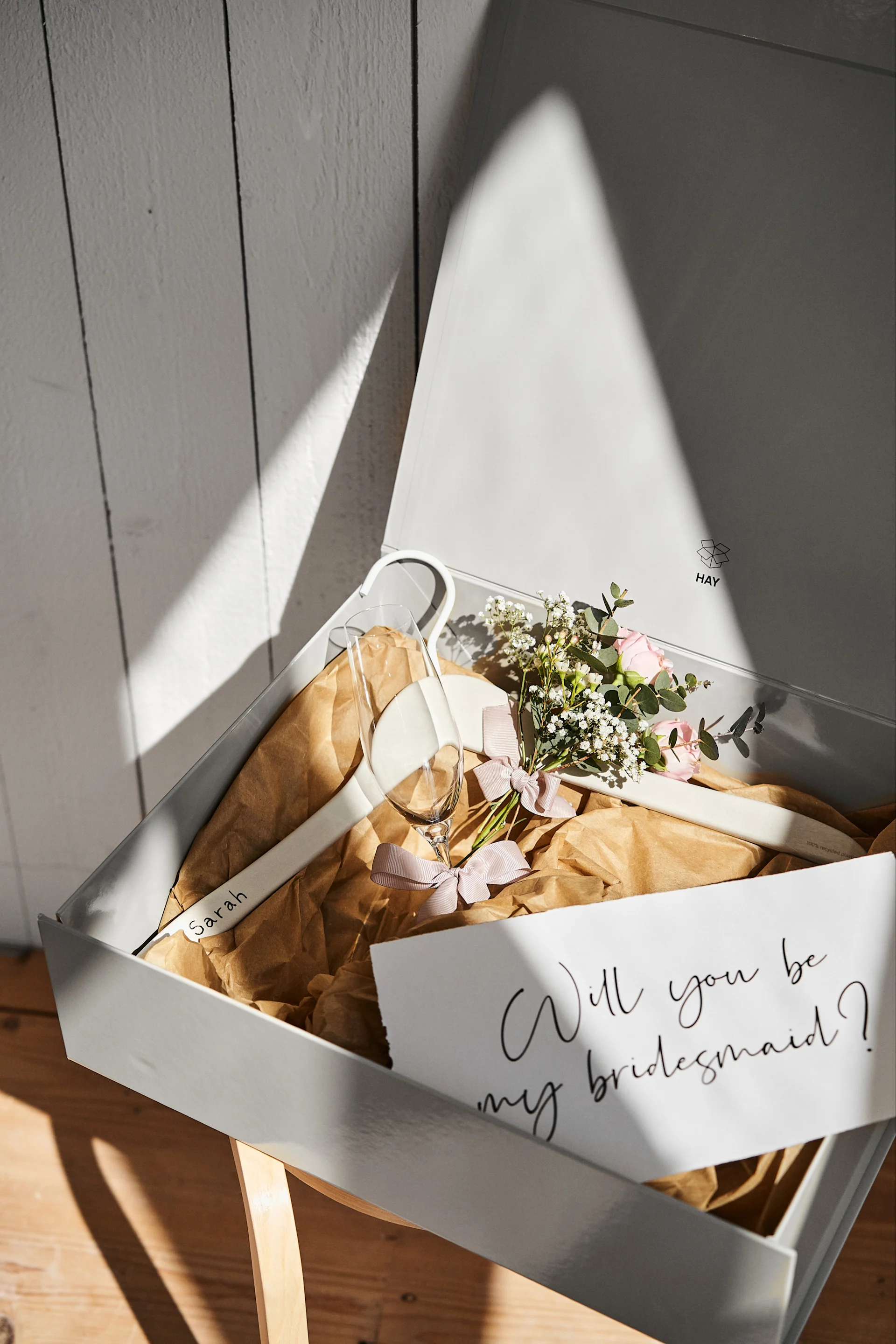 Bliv inspireret af disse unikke bryllupsidéer som denne personlige brudepigekasse i en grå opbevaringskasse fra HAY med en personlig bøjle til kjolen og et champagneglas til at fejre med.