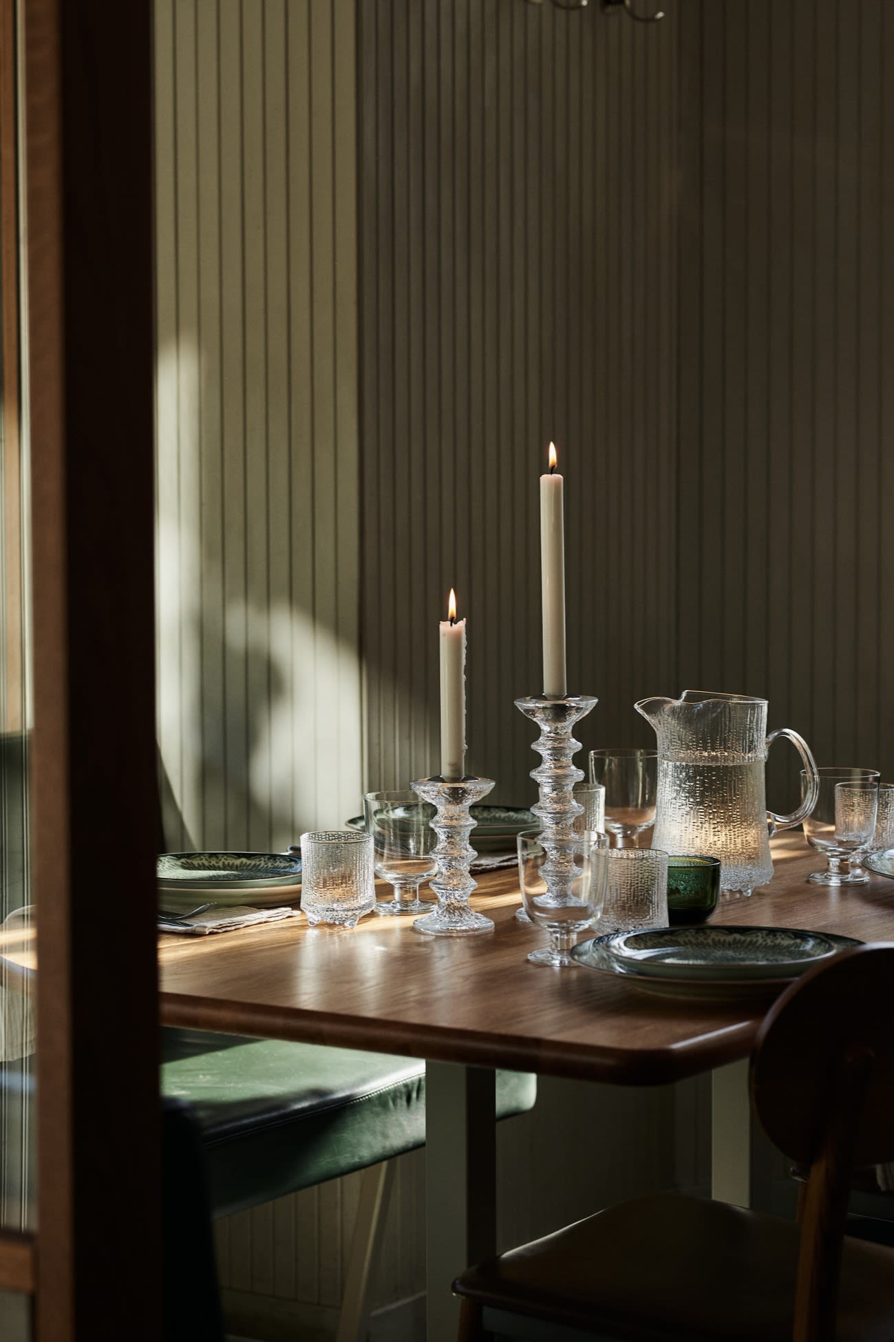 Her ser du en borddækning i et restaurantmiljø med grove lysestager i glas og matchende vandkande.