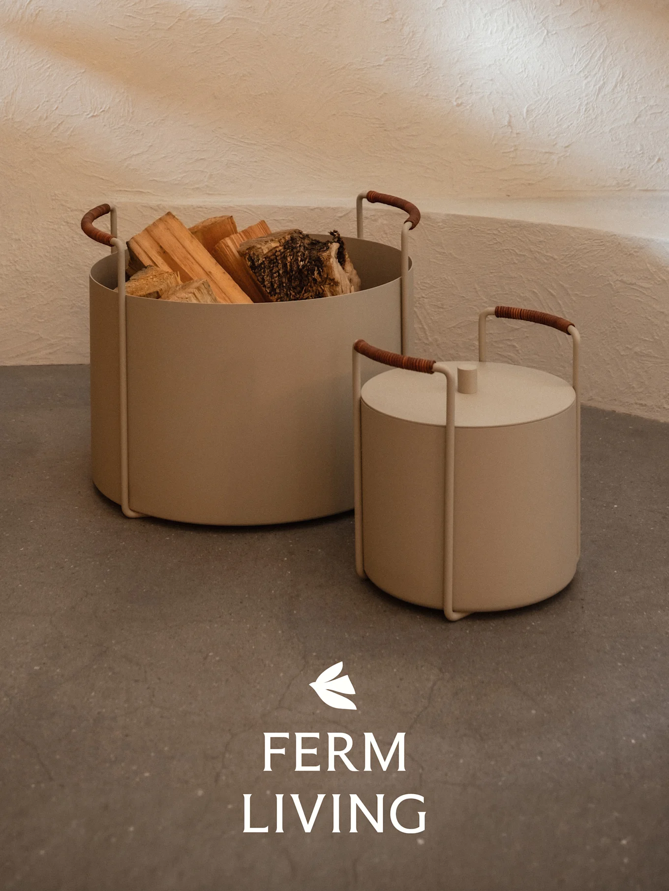 To beige cylindriske beholdere, den ene med brænde og den anden med låg, med brunindpakkede håndtag på et betongulv.