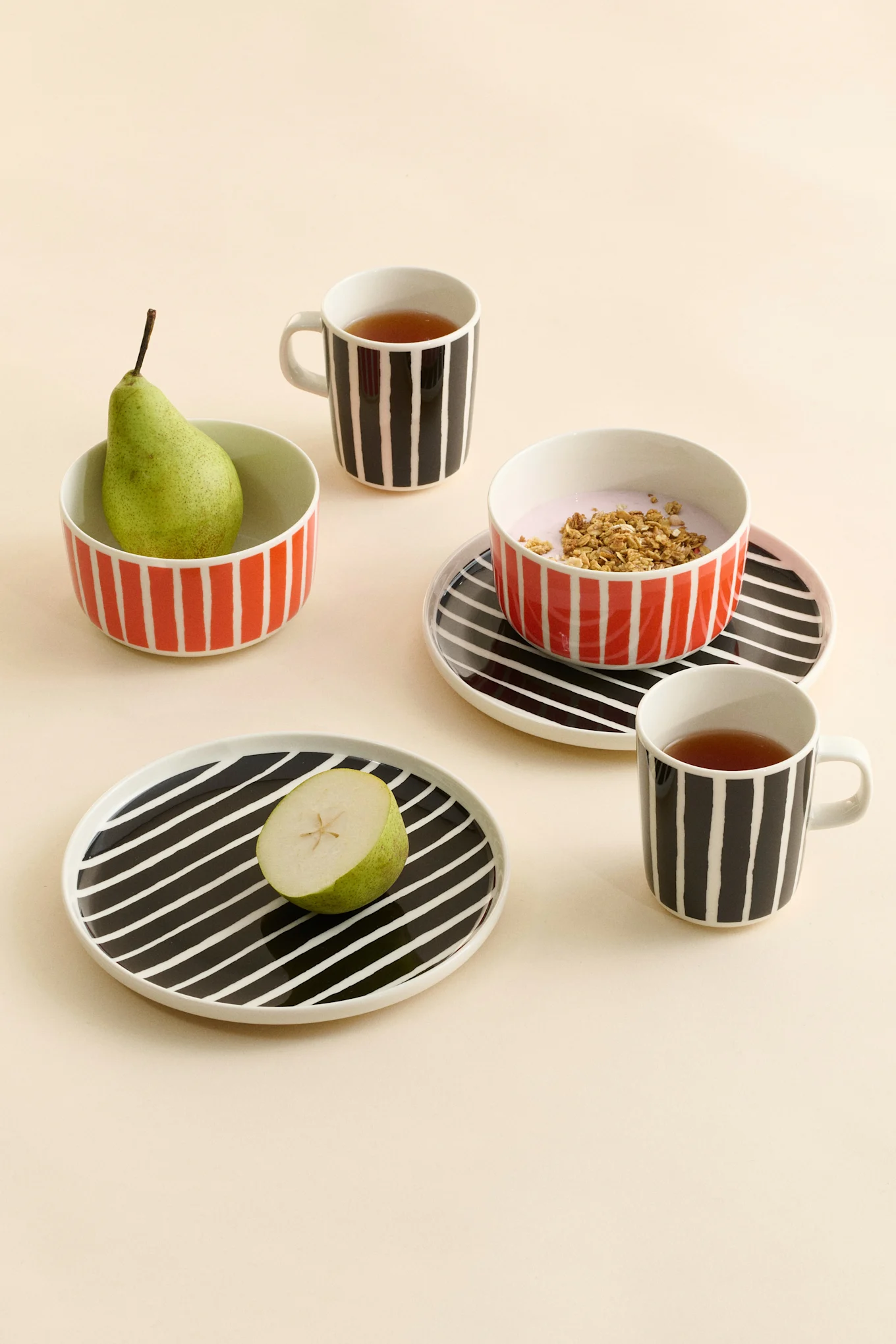 Stribede keramiske krus med te, skåle med pære og yoghurt med granola, og tallerkener med en halv pære.