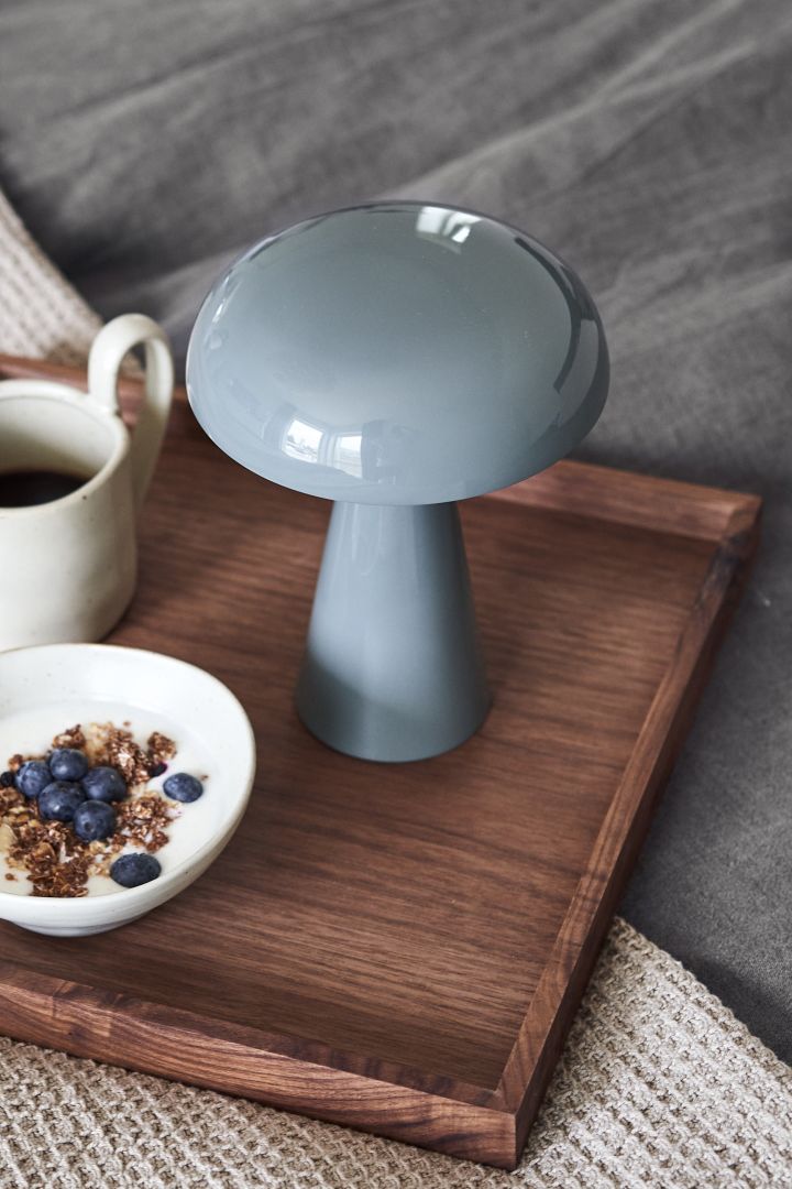Den portable og trådløse Como lampe i stone blue fra &Tradition står på et morgenmadsfad.