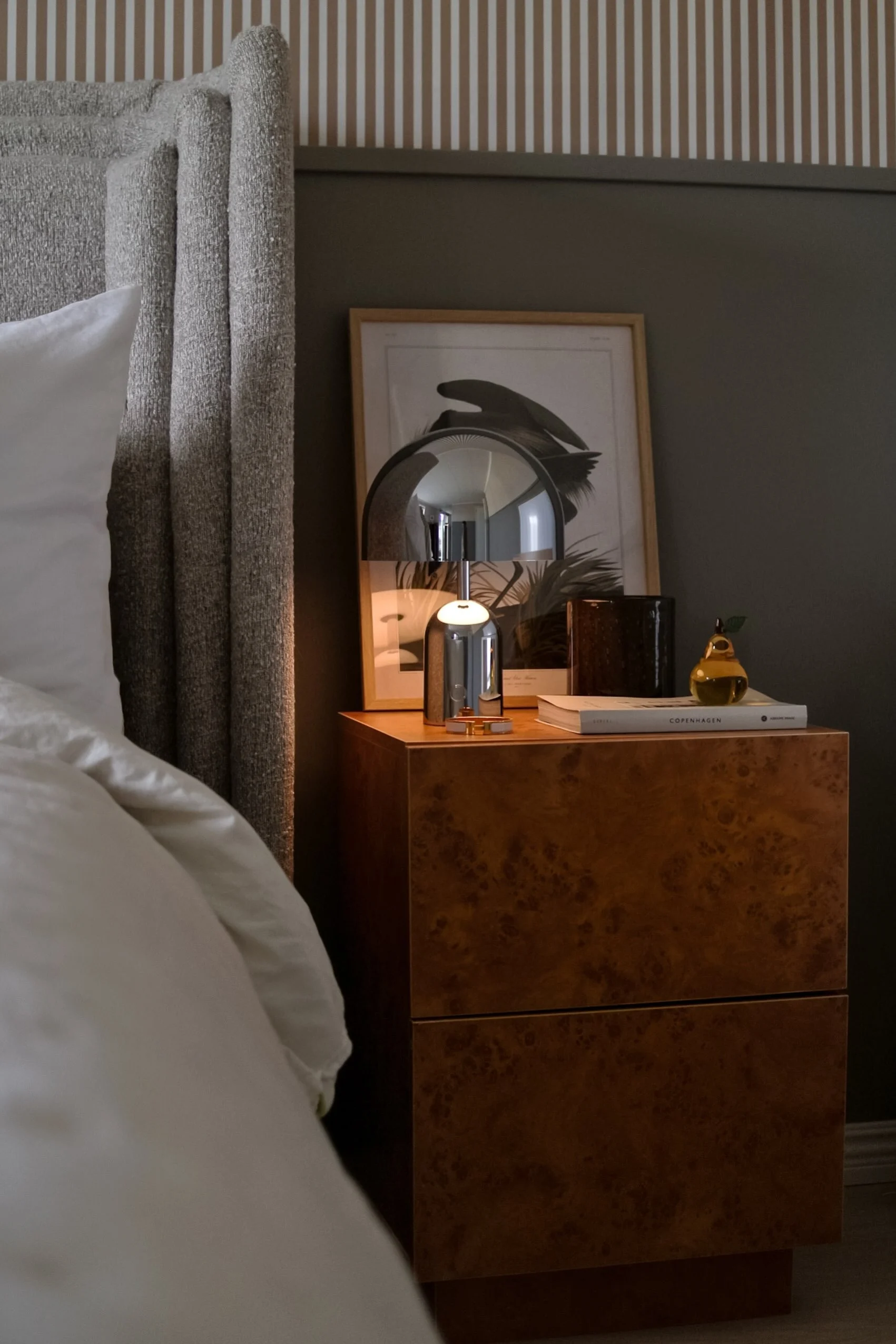 Et moderne spisestue med et bord dækket med hvide tallerkener, klare glas, en vase med hvide liljer og et højt lys, alt under en sort lysekrone med flere niveauer og fritlagte pærer.