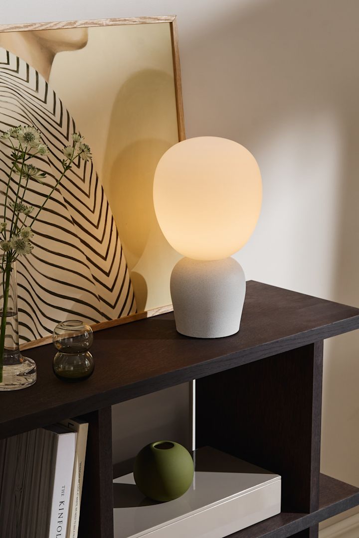Brug forskellige bordlamper, væglamper og loftlamper for at oplyse spisestuen. Her kan du se bordlampen Buddy med en lampeskærm i frostet glas fra Belid.