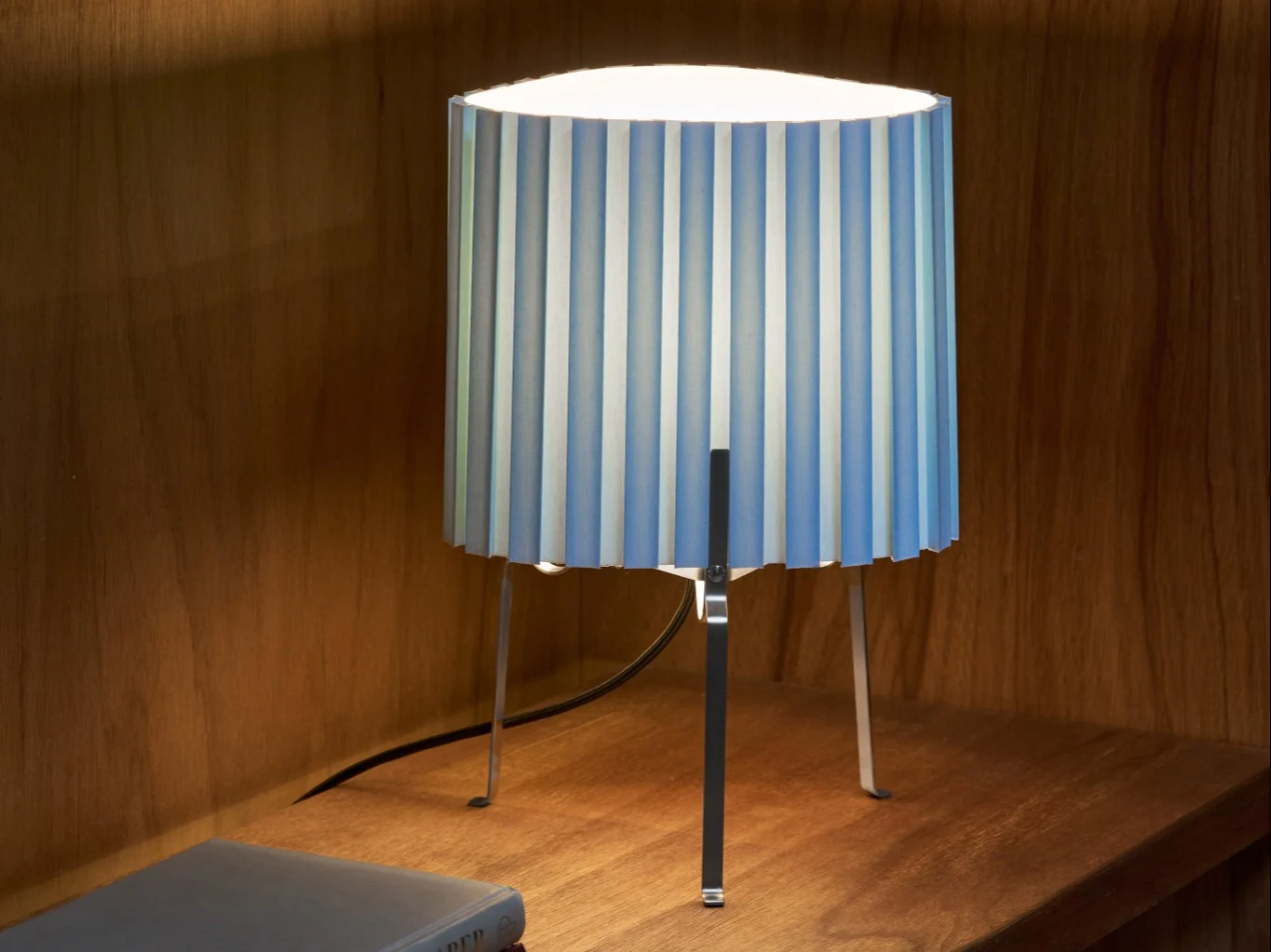 Bordlampe med plisseret blå- og hvidstribet skærm på en træhylde, der lyser området op.
