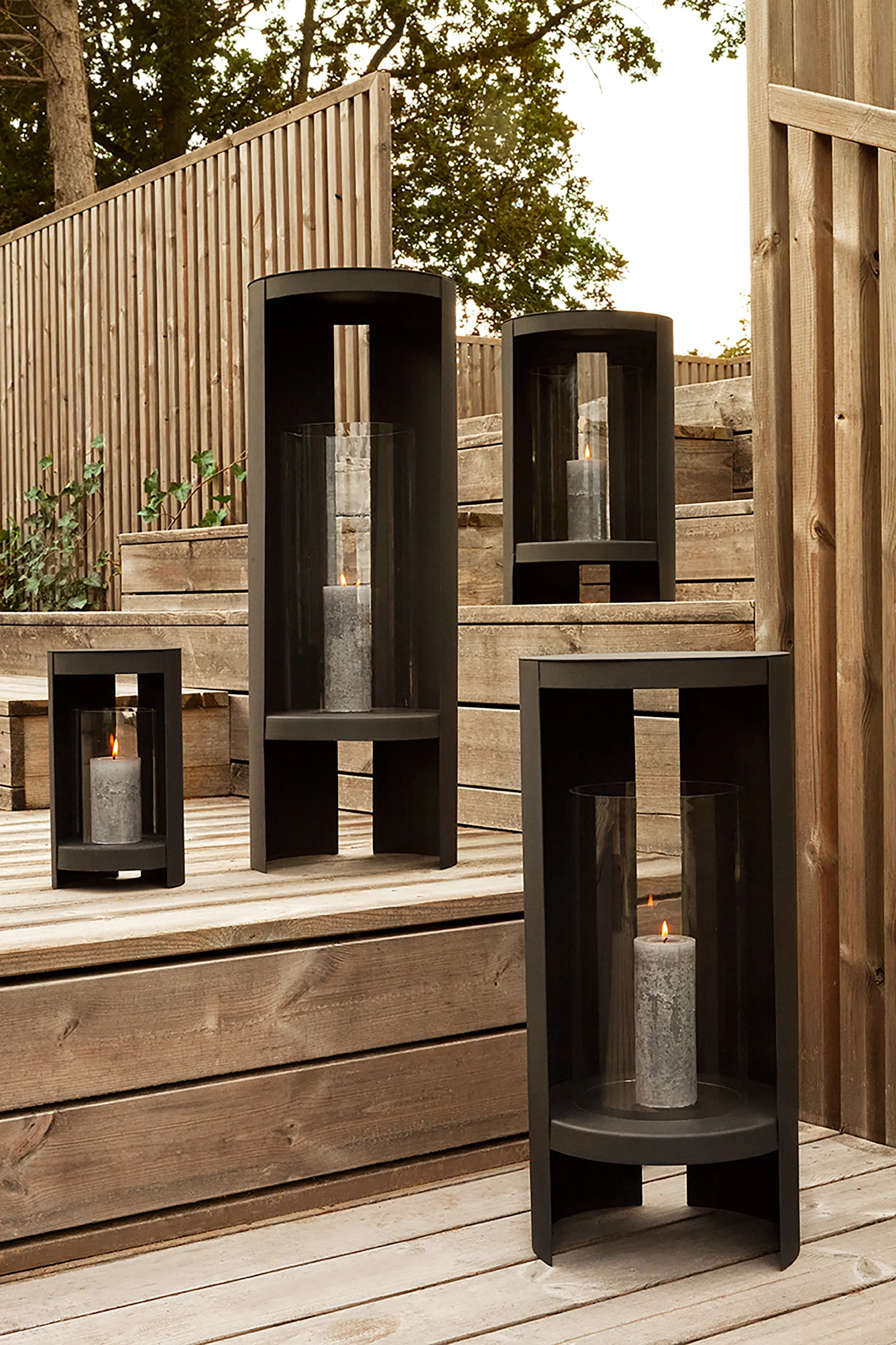 Lanterner og lygter til udendørs brug - her ses Oro-lanternen fra AYTM i sort og i forskellige størrelser stående på en trætrappe i en have.